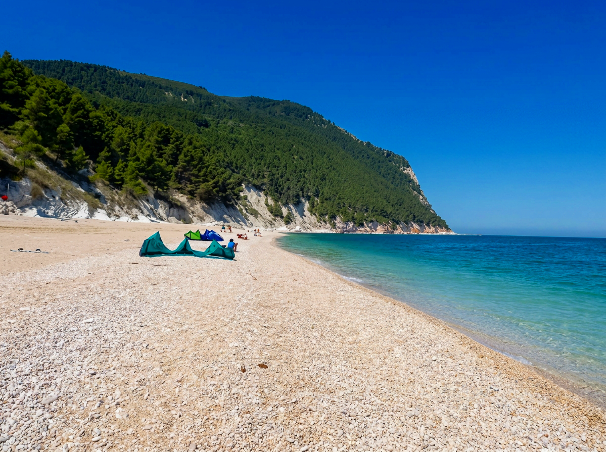Wild pebble beach and clear turquoise water beneath the forested cliffs of Monte Conero at Spiaggia dei Sassi Neri, Le Marche, Italy