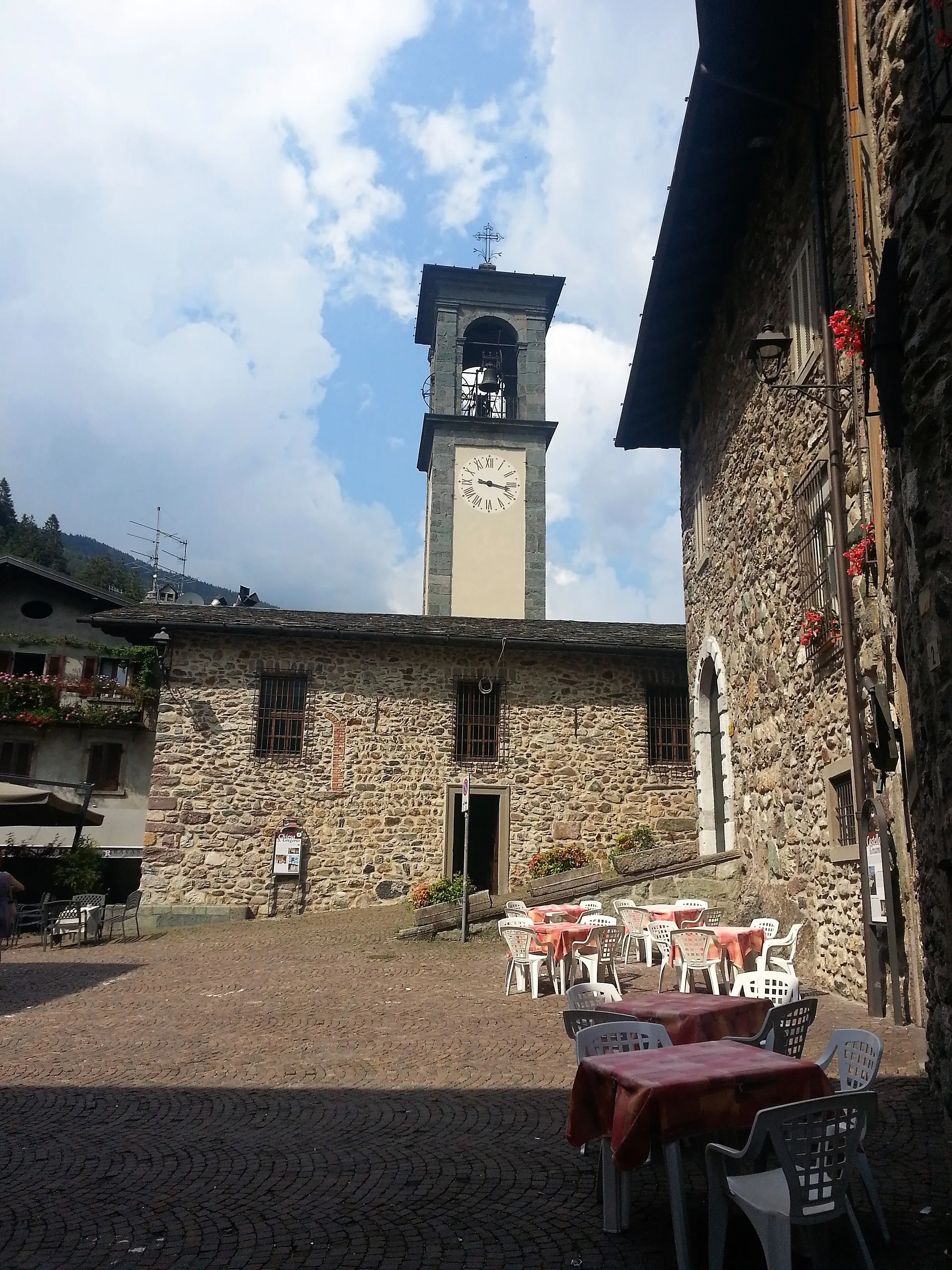 San Gregorio church and its clock tower beside café tables in Piazza Dante, Gromo.