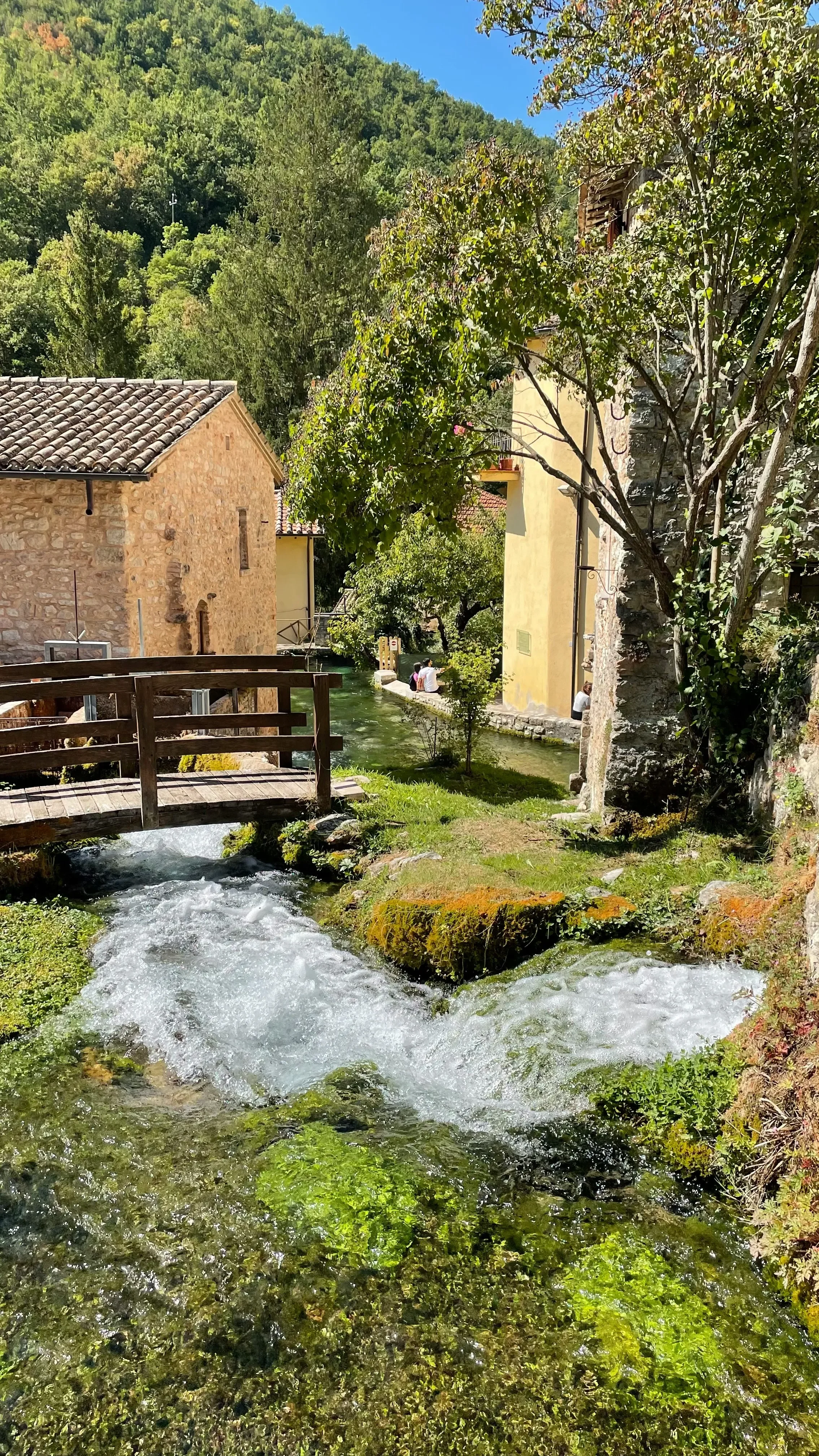 Clear water cascading beneath a wooden bridge between stone houses in Rasiglia