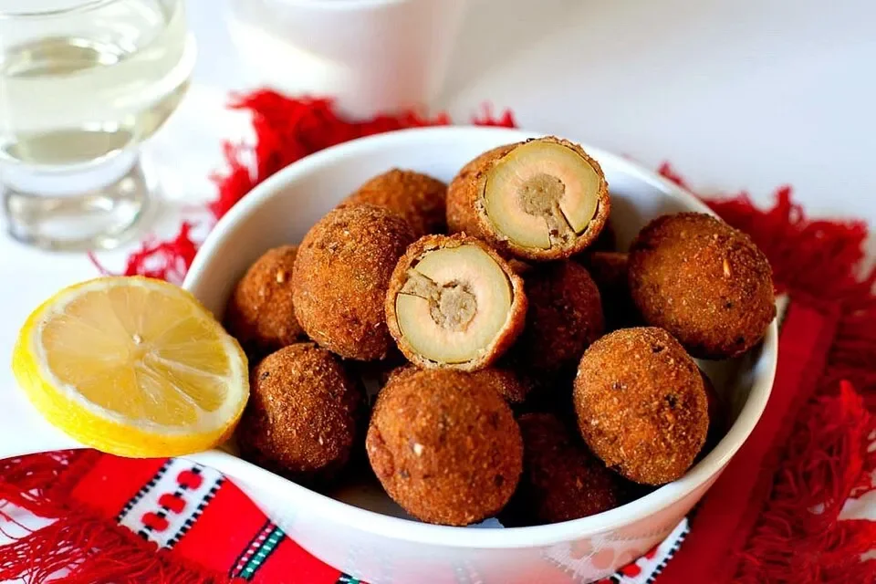 Golden breaded olive all’ascolana in a white bowl, with halved stuffed olives and a lemon wedge