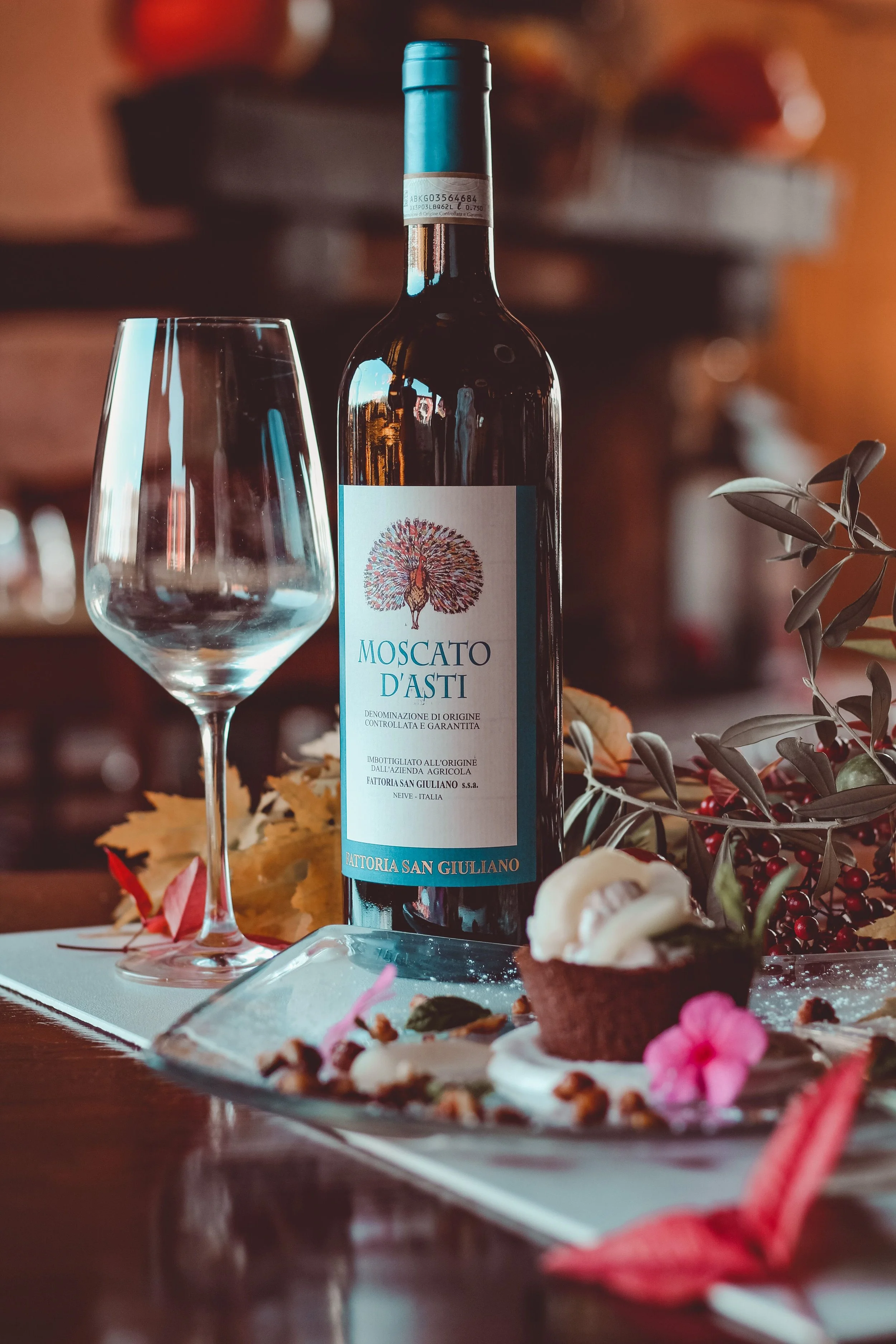 A bottle of Moscato d’Asti beside an empty wine glass and a plated dessert.