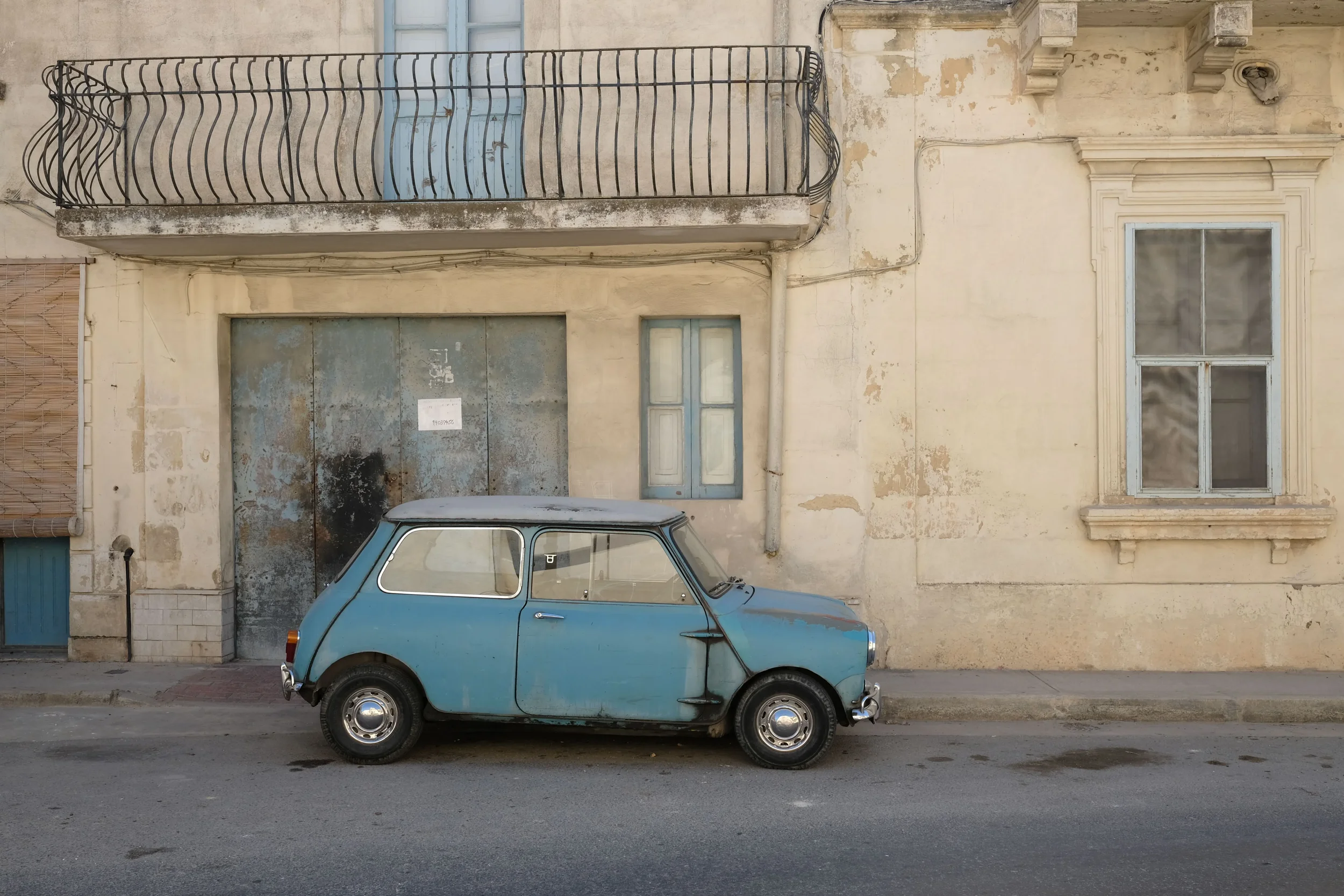 Vintage blue car parked in front of an old building on a quiet street in Puglia, southern Italy