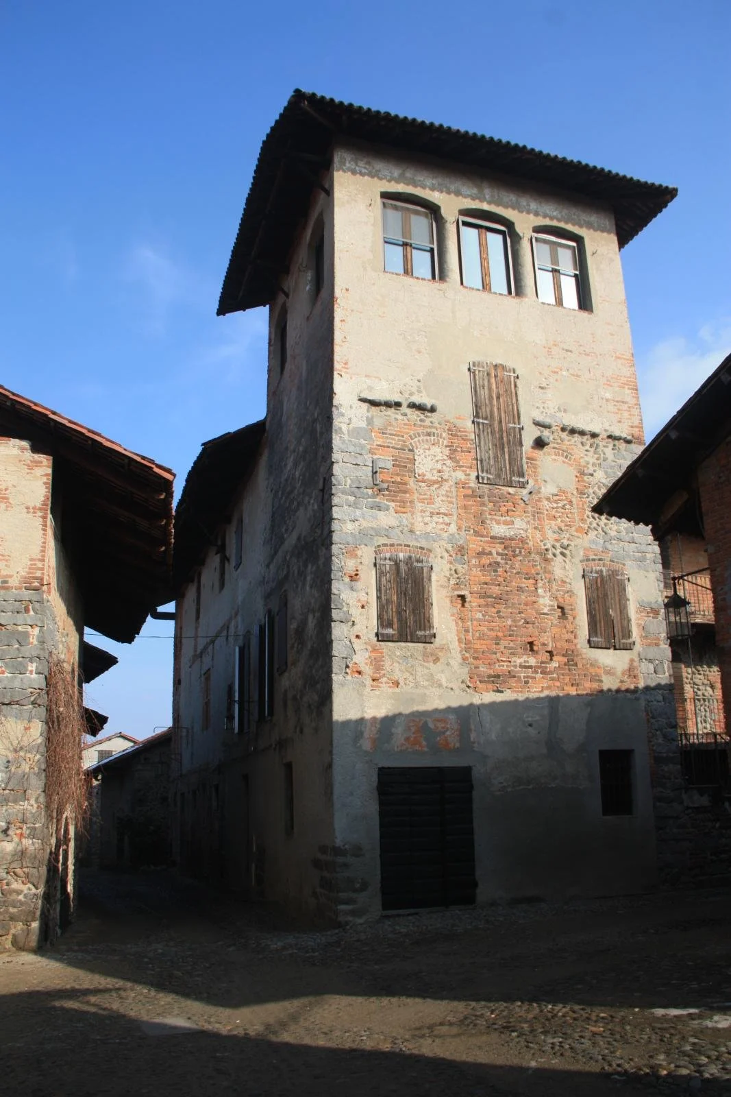 Tall stone and brick building beside a cobbled lane inside Ricetto di Candelo