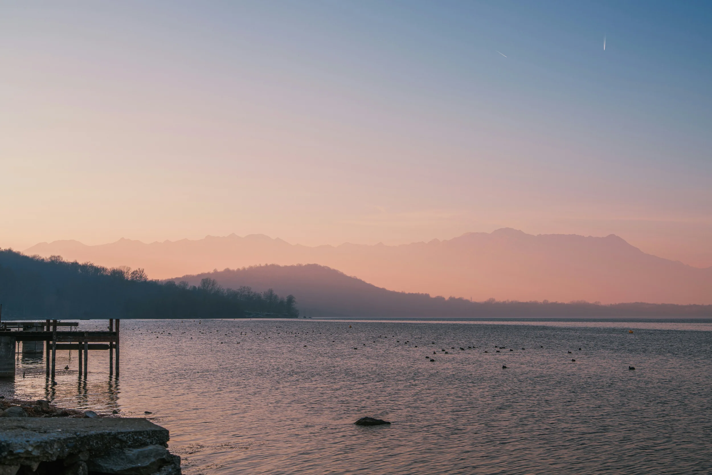 Sunset over Lago di Viverone, with a small wooden jetty and distant mountains beneath a pink sky, Piemonte, Italy.