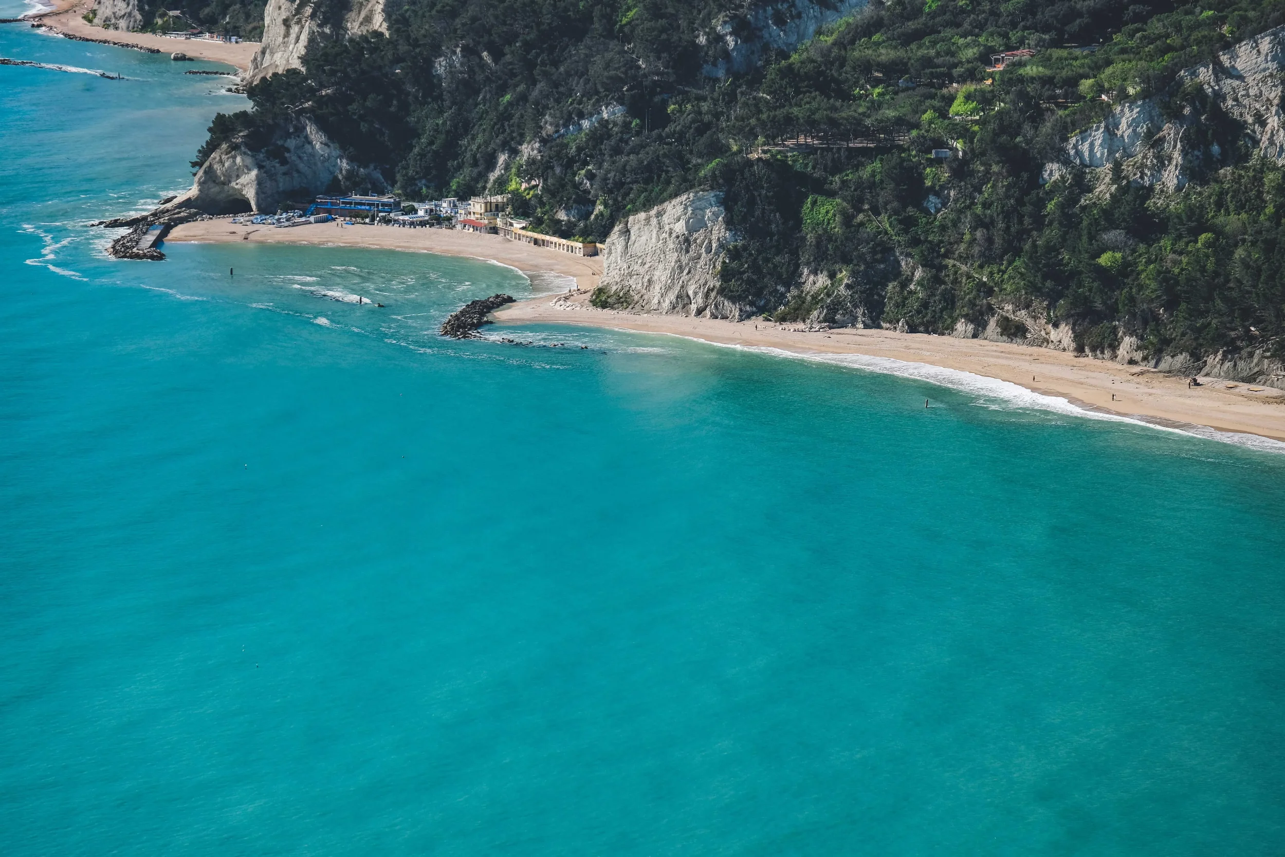 Aerial view of a turquoise bay with a sandy beach, rocky cliffs and lush Mediterranean vegetation along the Puglia coastline in southern Italy