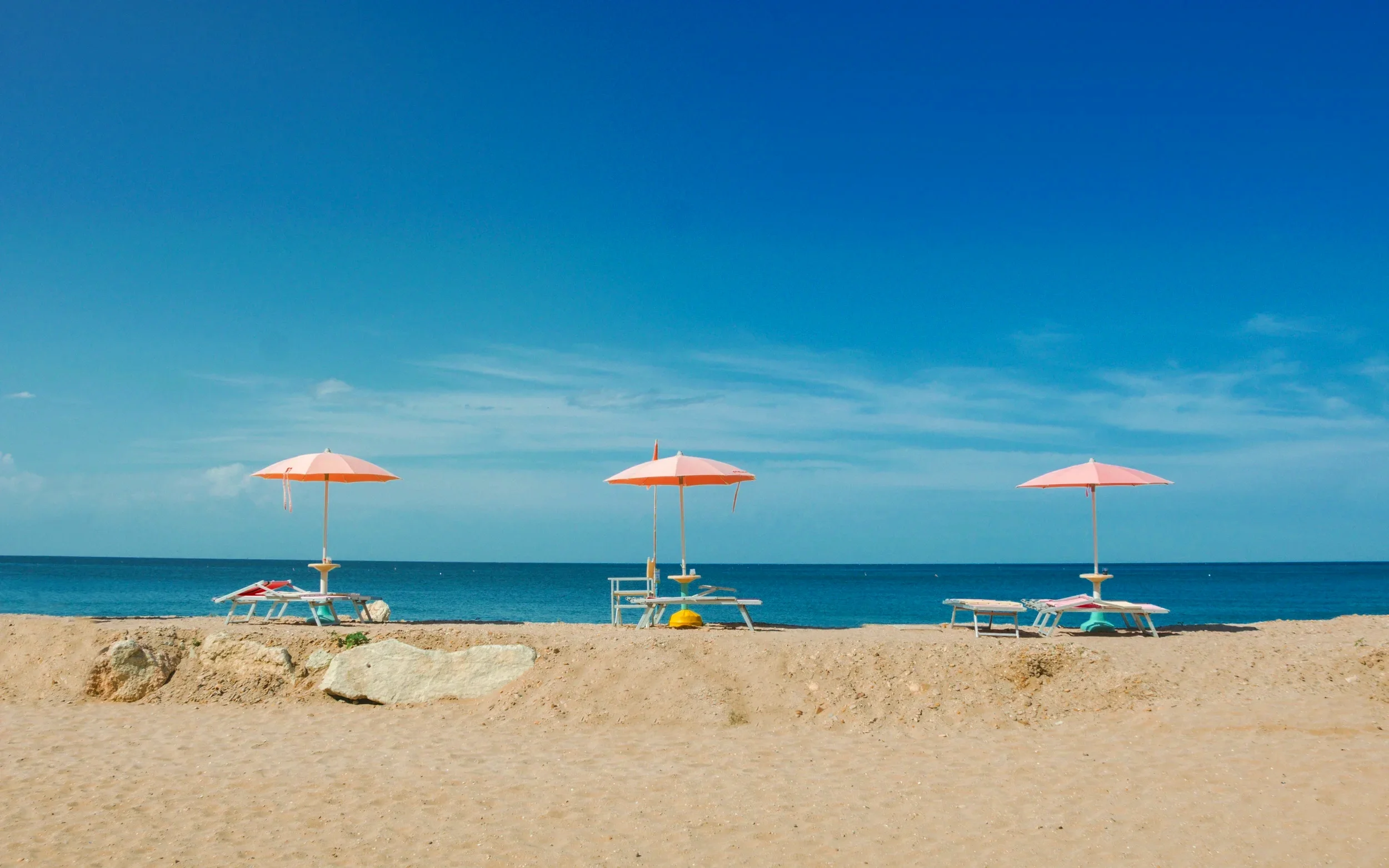 Pink parasols and sun loungers on a sandy beach overlooking the calm blue sea in Tuscany