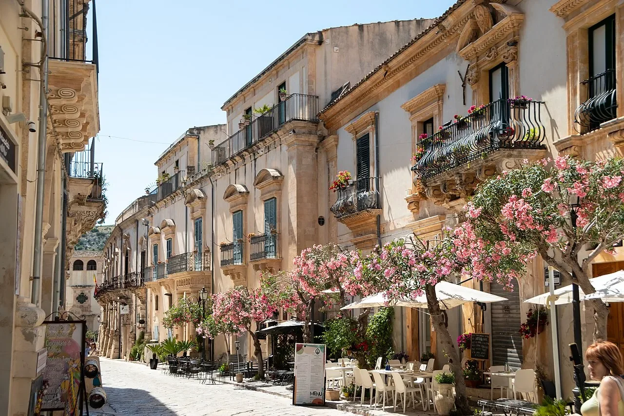 Baroque façades, wrought-iron balconies and flowering trees along Via Francesco Mormino Penna in Scicli