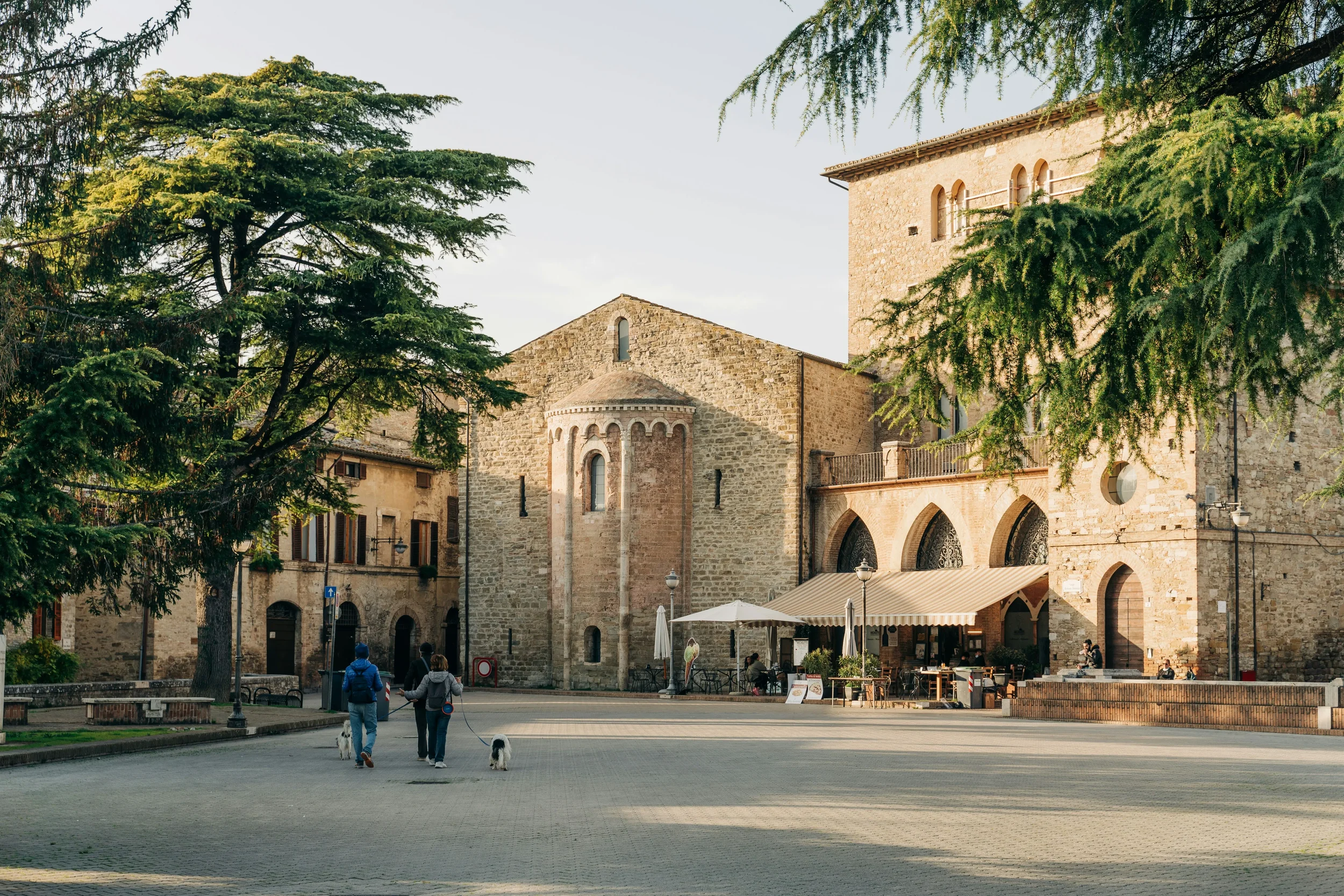 Piazza Silvestri in Bevagna, with medieval stone buildings, café tables and trees around the square