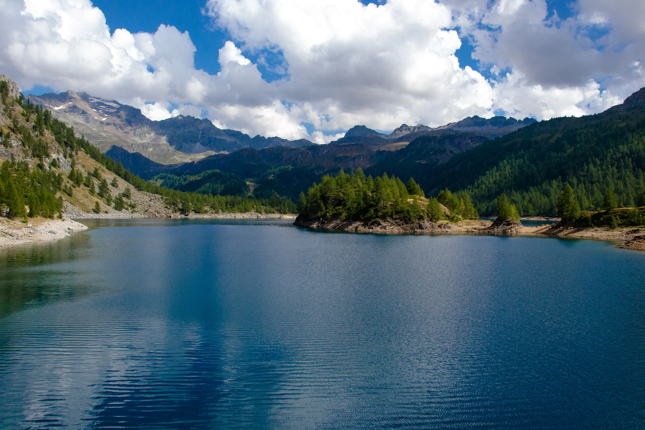 Lago di Devero viewed from the dam, with wooded shores and mountains beyond.