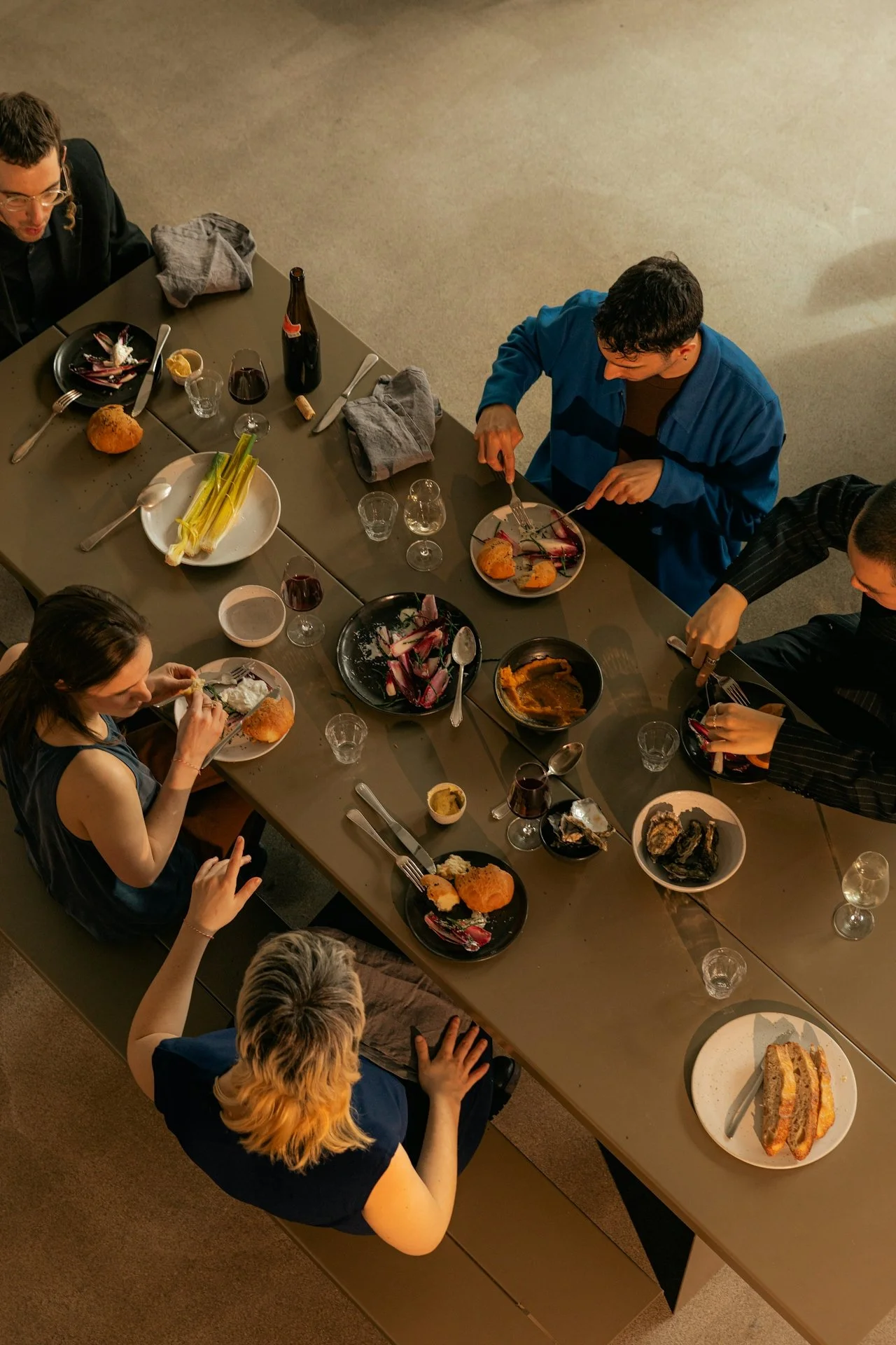 People sitting at a dining table enjoying a meal with various dishes and drinks, viewed from above.