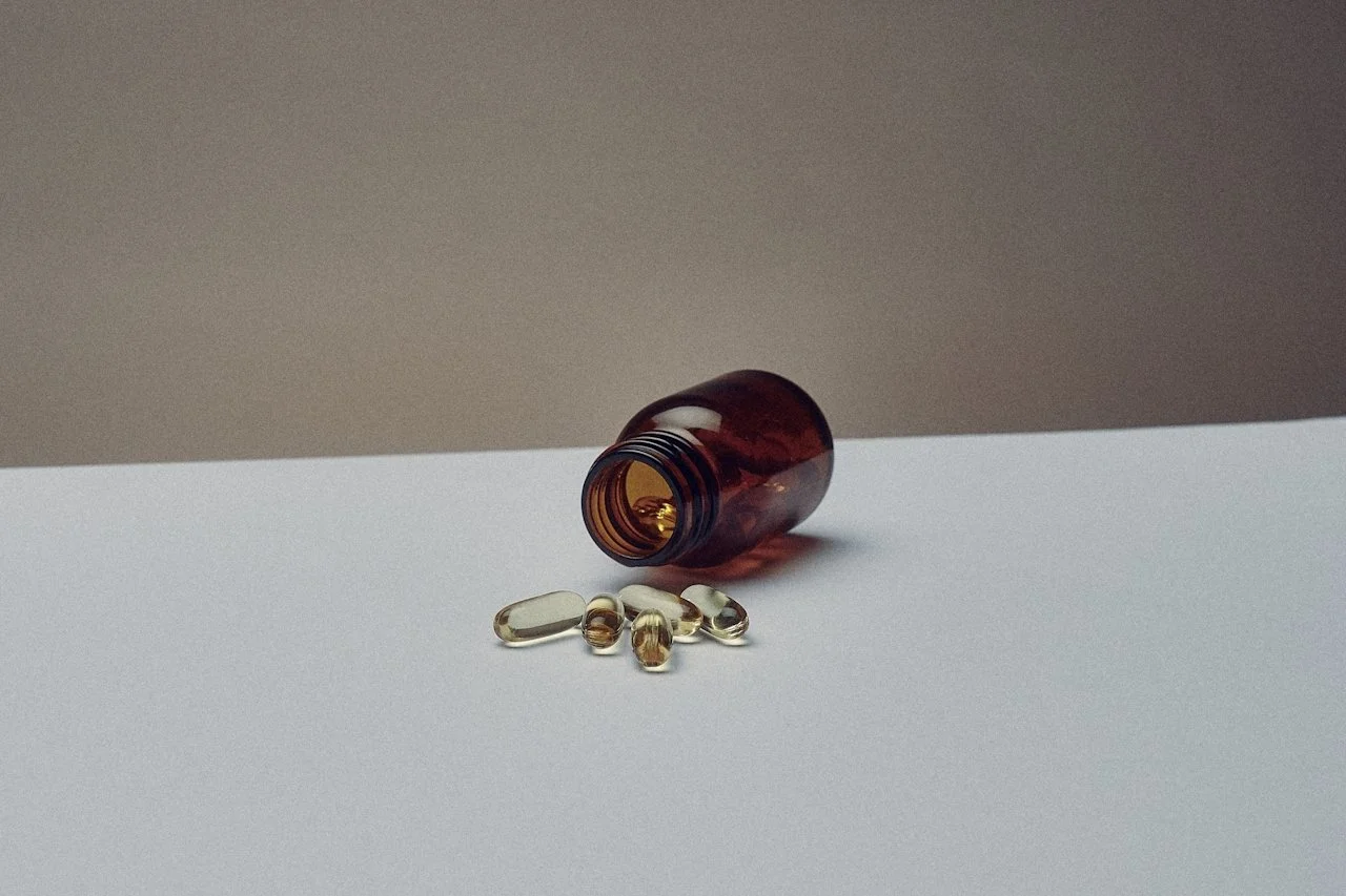 An open amber pill bottle lying on its side with several clear capsule pills spilled onto a white surface.