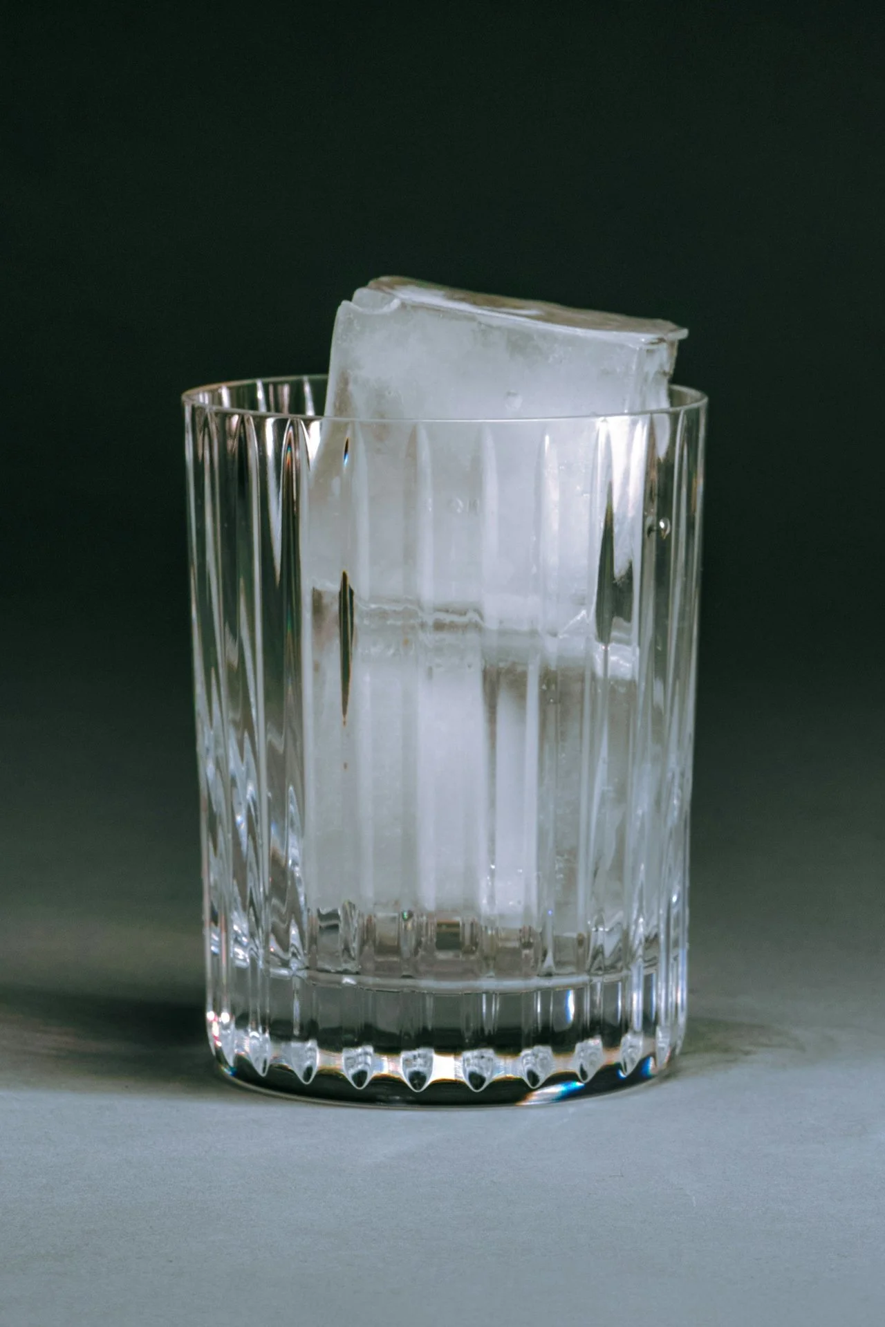 A clear glass with vertical ridges on its sides, filled with large ice cubes against a dark background.
