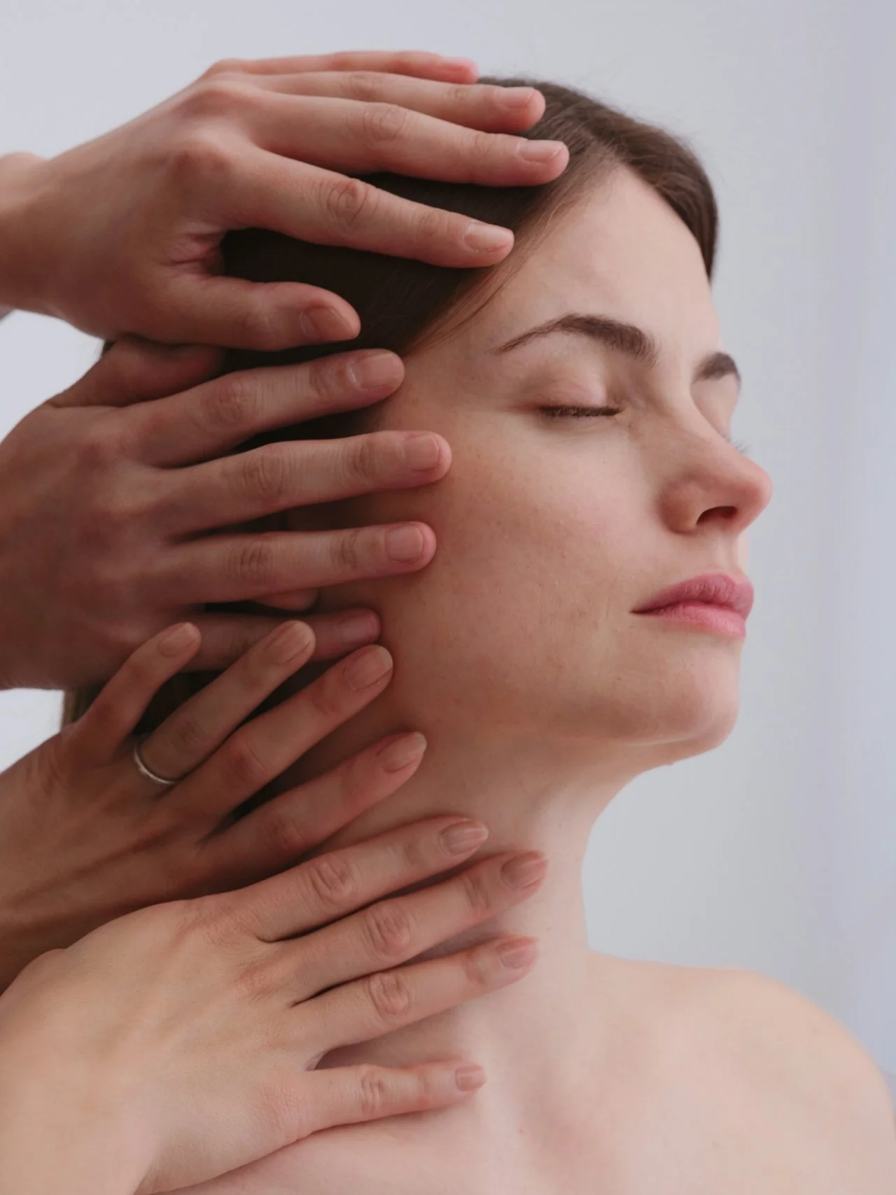 A woman with closed eyes and relaxed facial expression receiving a head and neck massage from multiple hands.