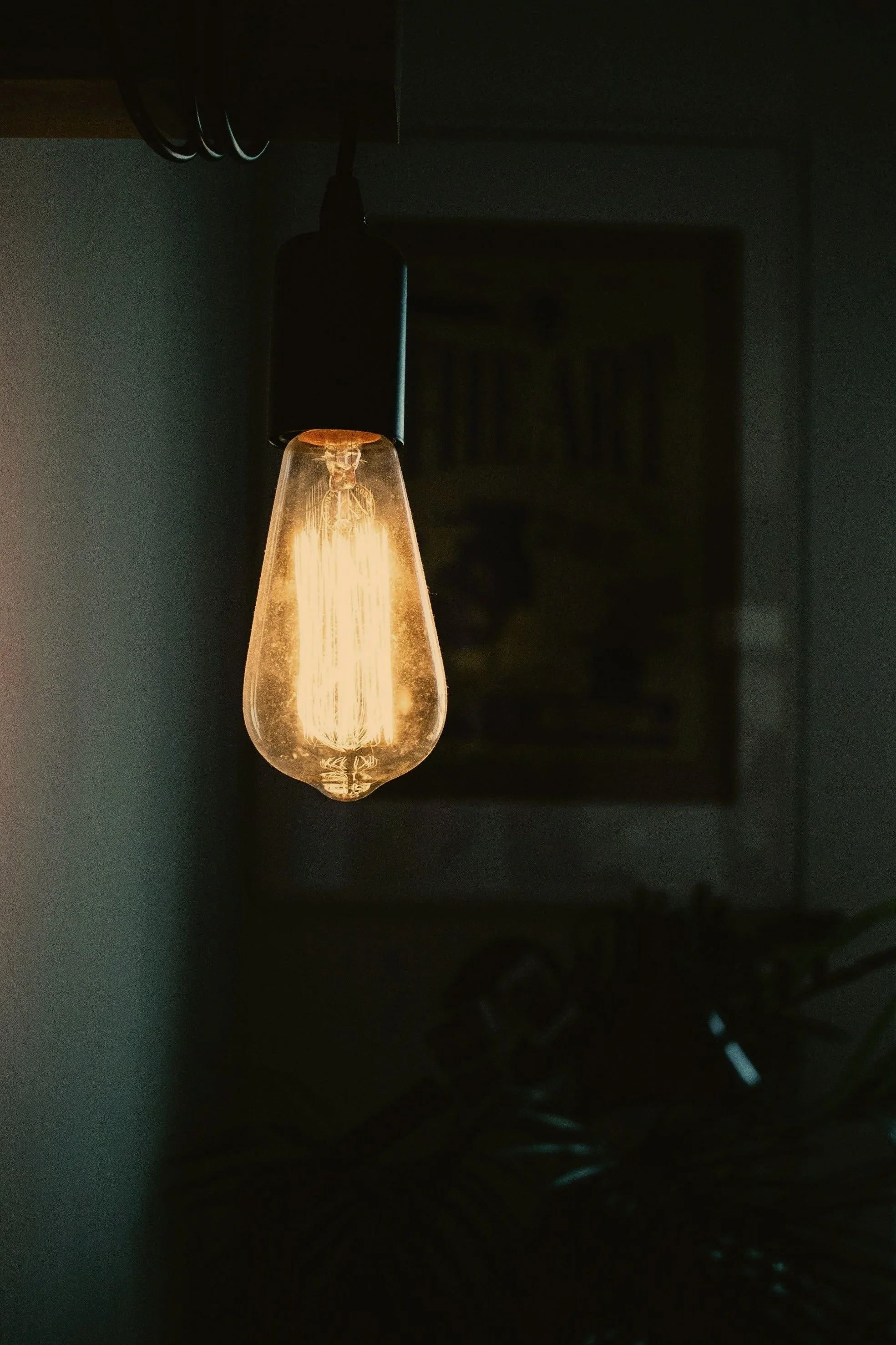 A glowing vintage-style Edison light bulb hanging from a dark ceiling.