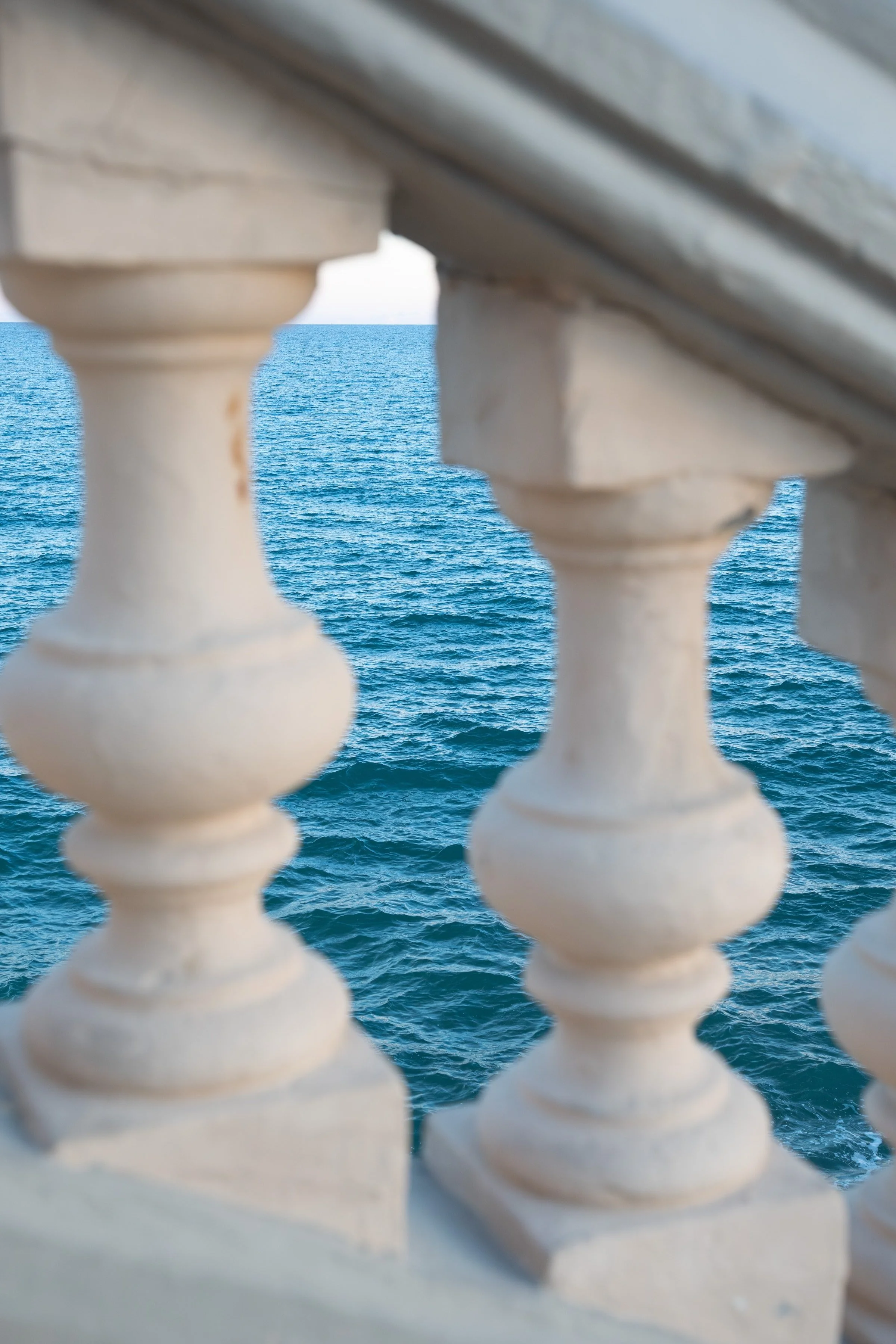 View of the blue ocean through a decorative white balustrade on a balcony or terrace.