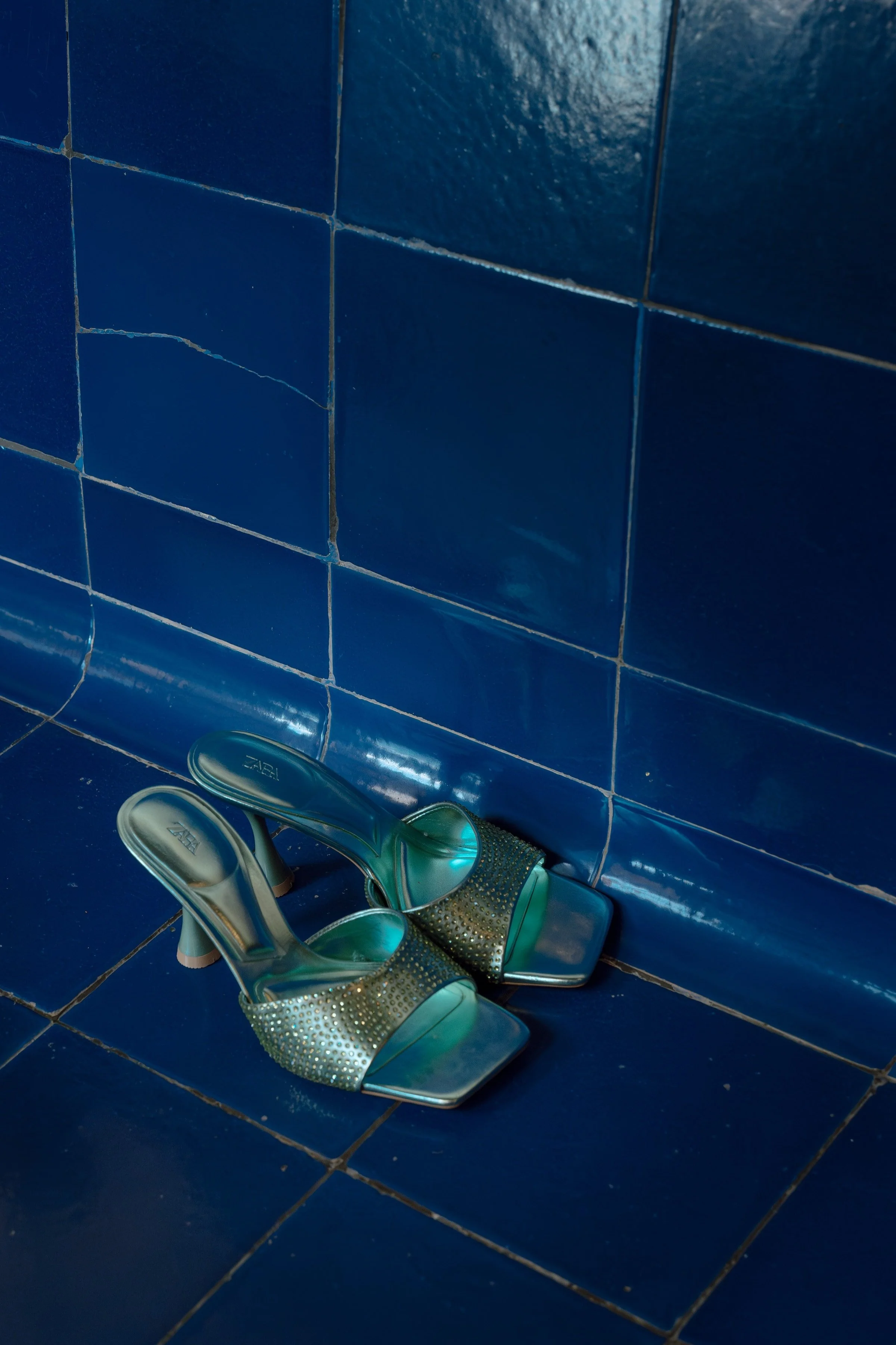 High heels shoes with open toes placed on a blue tiled floor and wall.