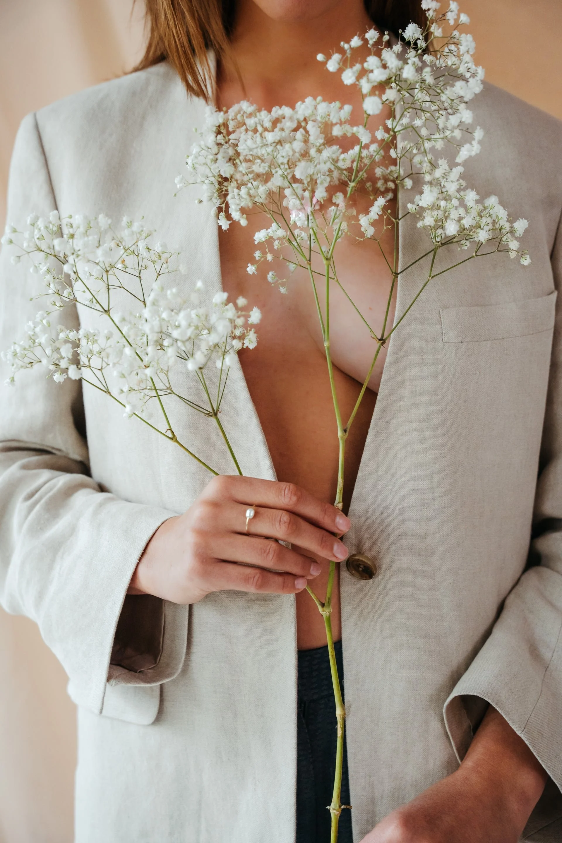 A woman holding a bunch of white baby's breath flowers while wearing a beige blazer.