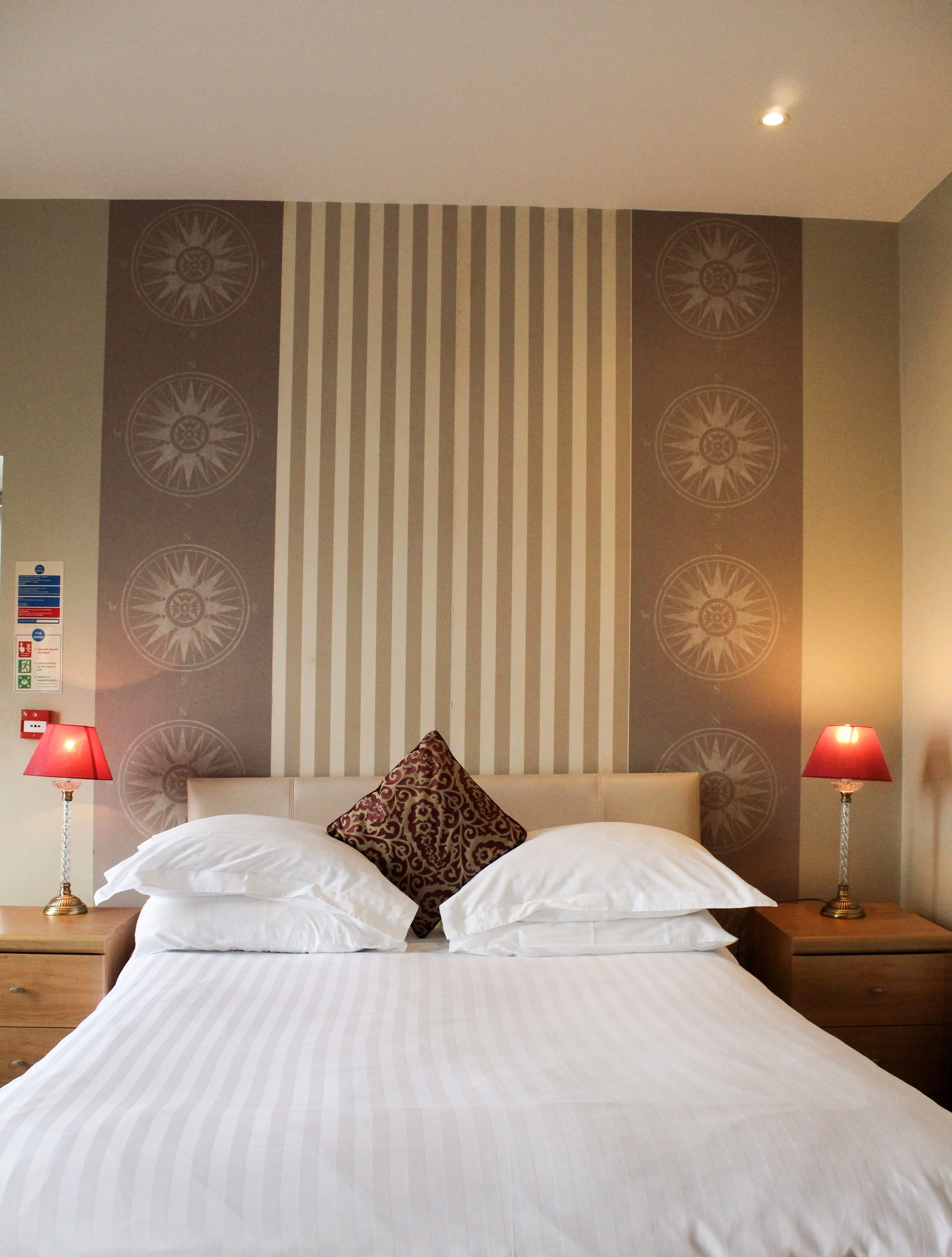 Large double bed with pillow in the middle. Nautical themed wallpaper