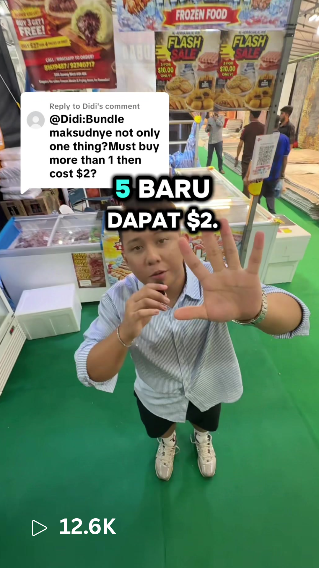 Young man in striped shirt reaching out with his hand at a market stall, with posters advertising frozen food and a man in the background surrounded by market supplies.