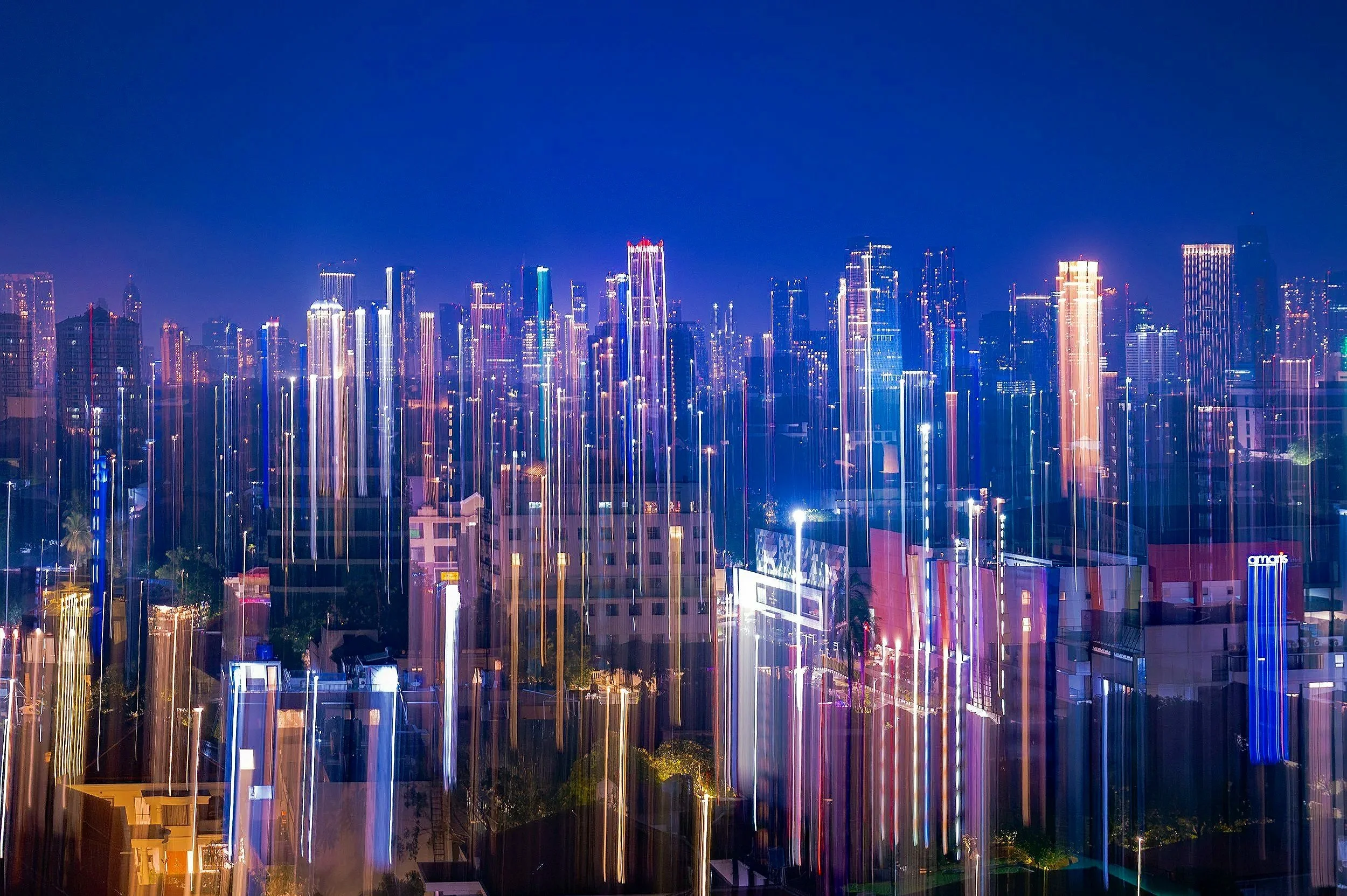 Nighttime cityscape of a modern city skyline with illuminated skyscrapers and light streaks from long exposure photography.