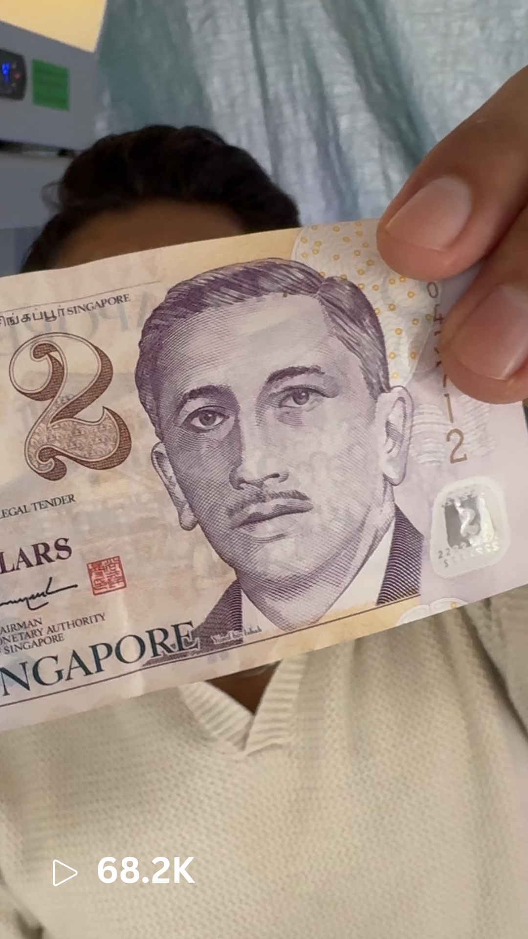 Person holding a two-dollar bill in front of their face, with part of their head and beige shirt visible.