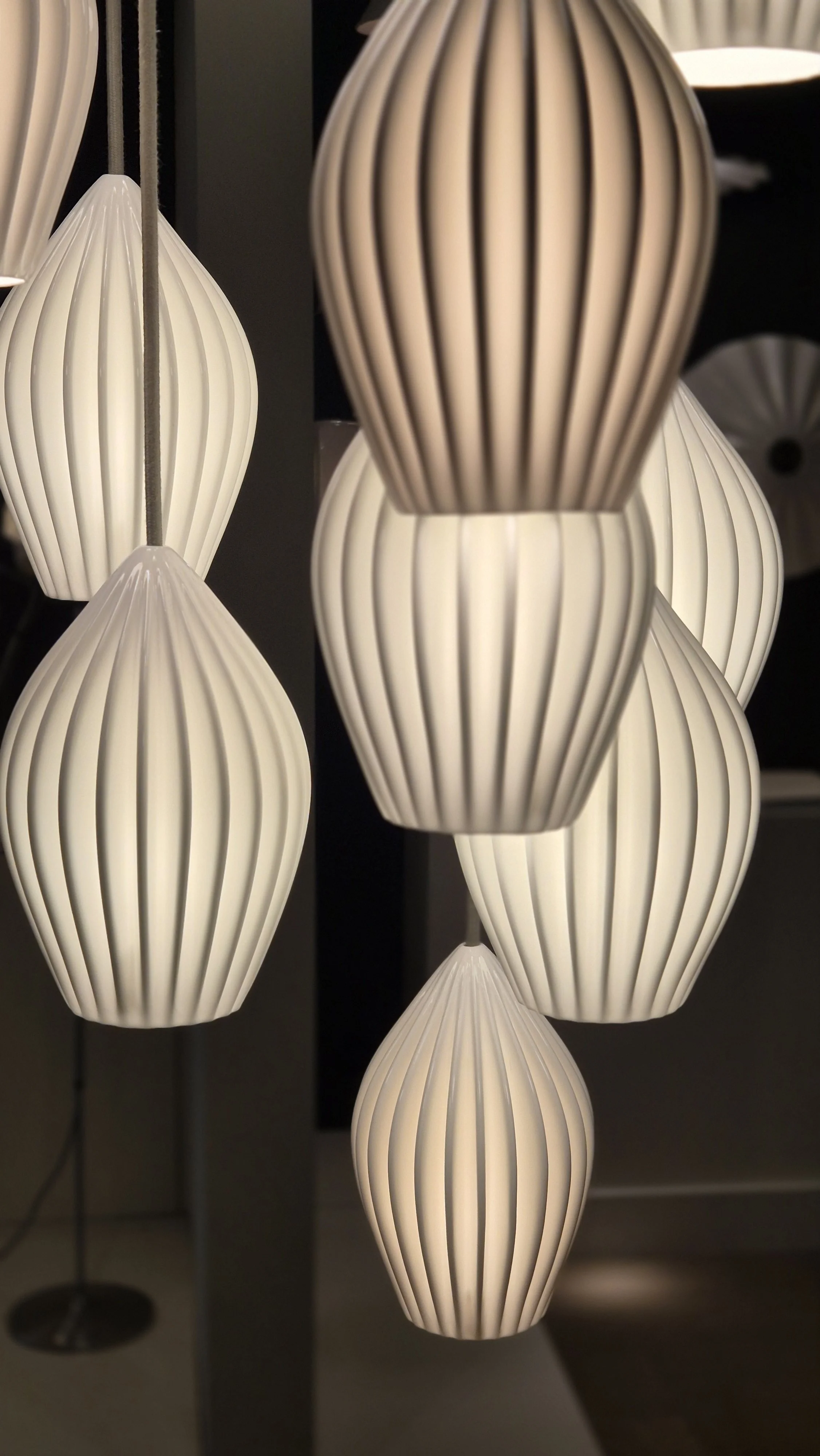 Multiple white, ribbed, tear-drop shaped pendant lights hanging from the ceiling, illuminated with a warm glow.