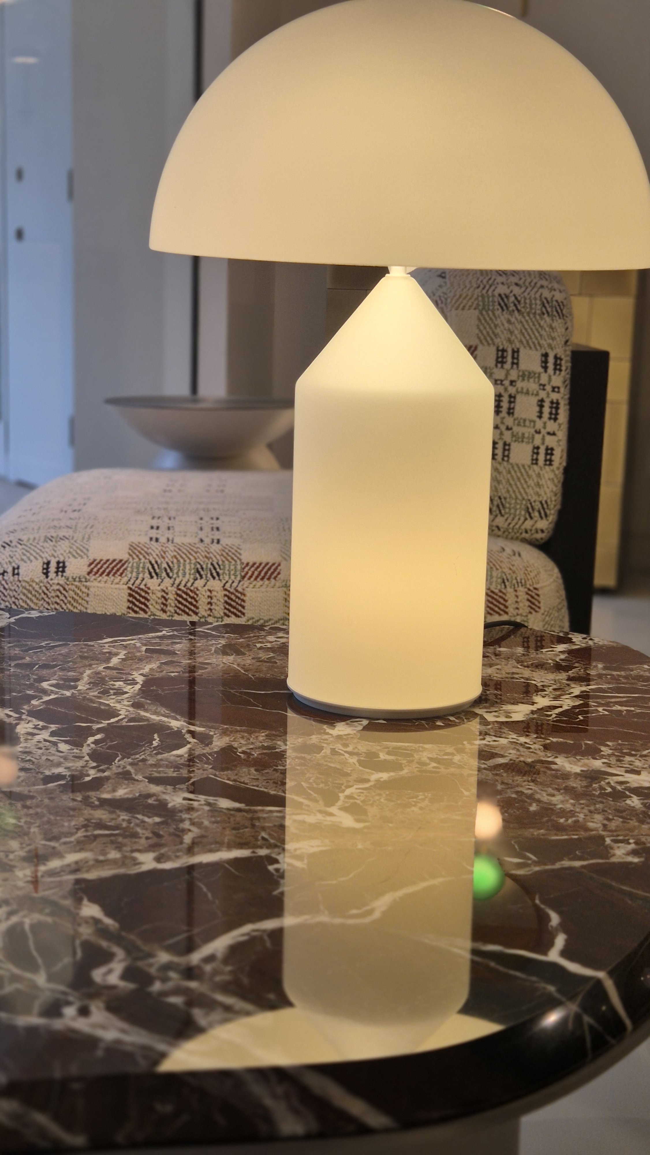 A modern table lamp with a cylindrical base and a dome-shaped shade, placed on a polished marble table in a cozy living room.