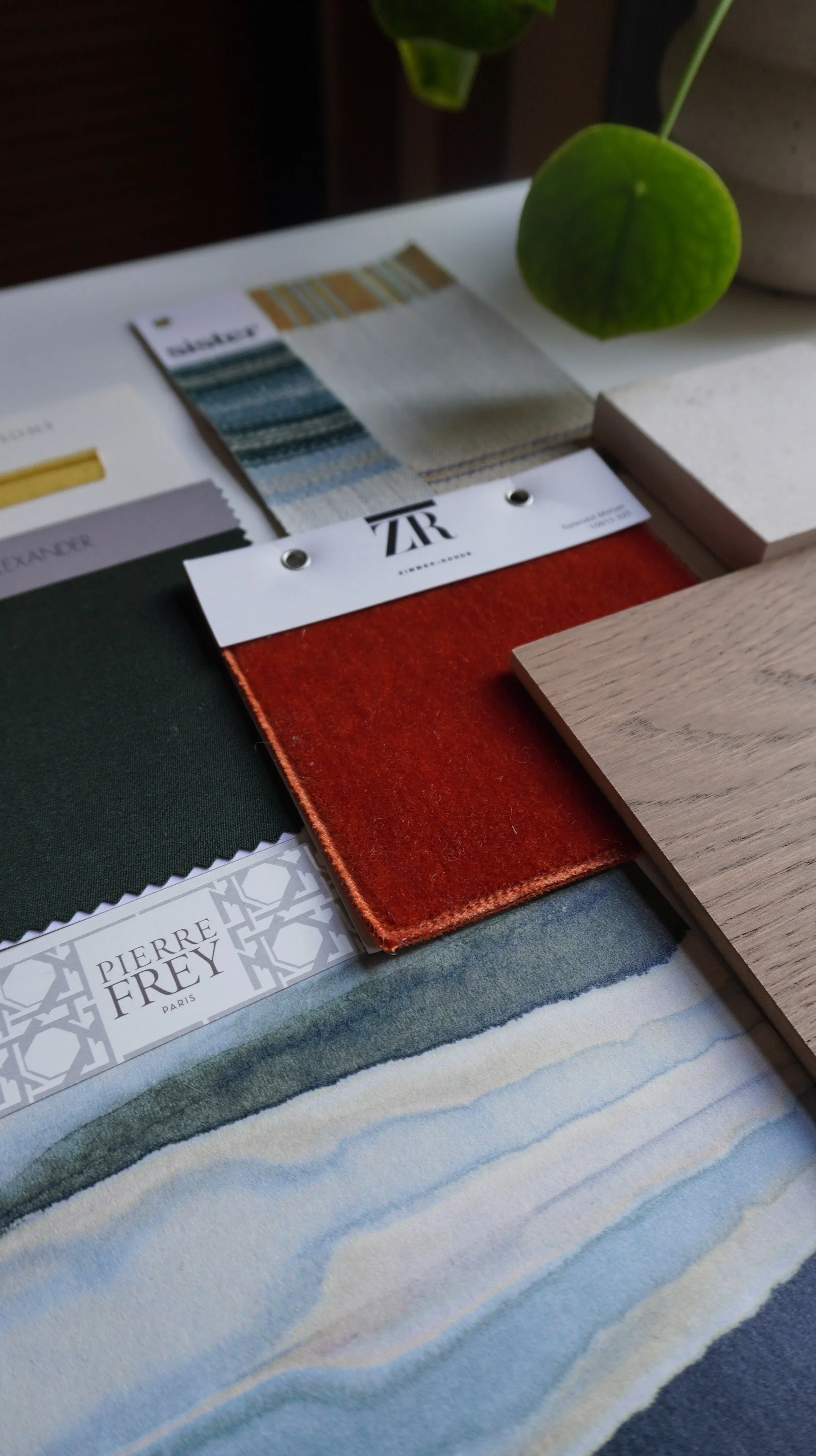Color palette and fabric samples on a striped cloth surface, with a green potted plant in the background.