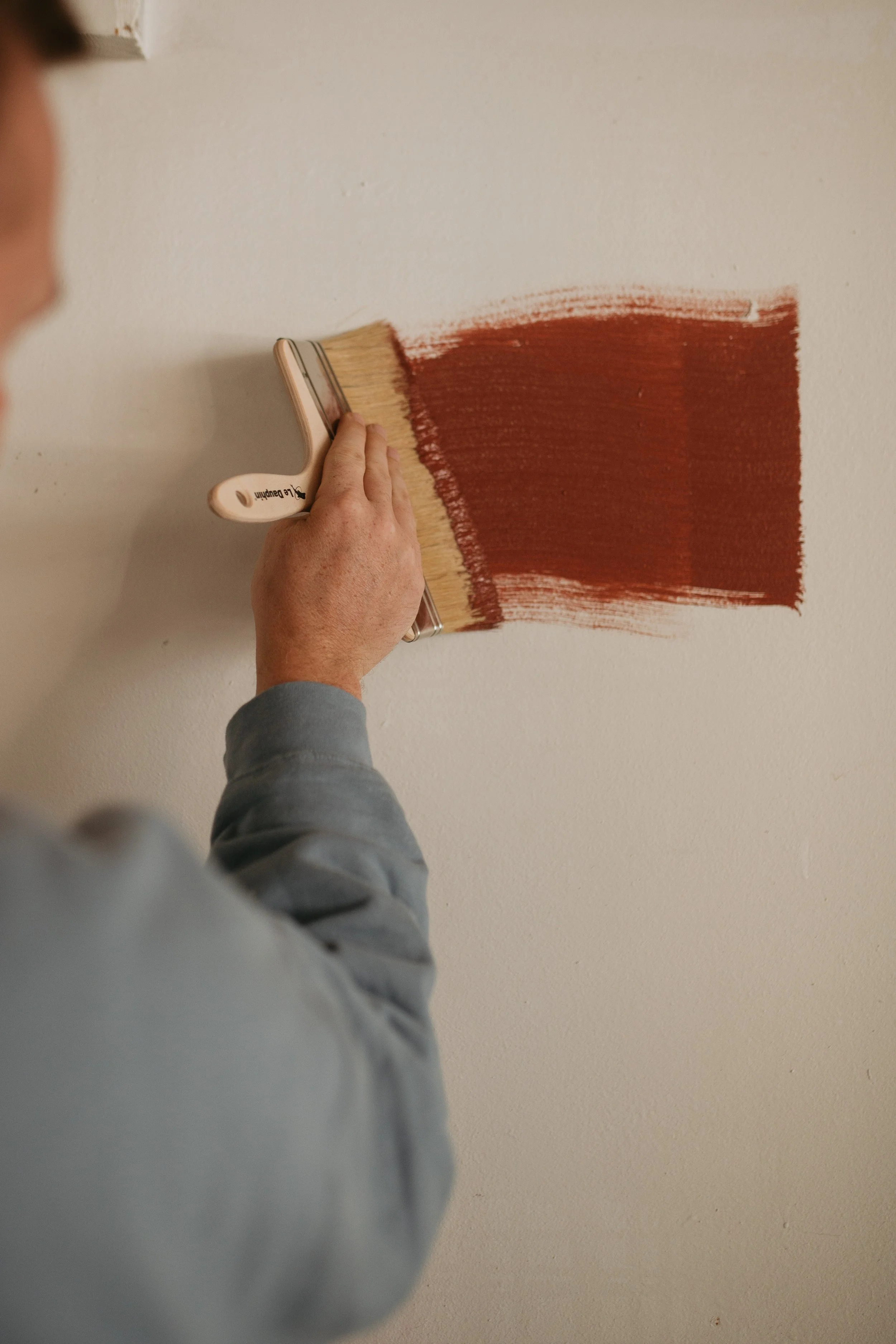 Une personne peint un mur blanc avec de la peinture marron à l'aide d'une brosse.
