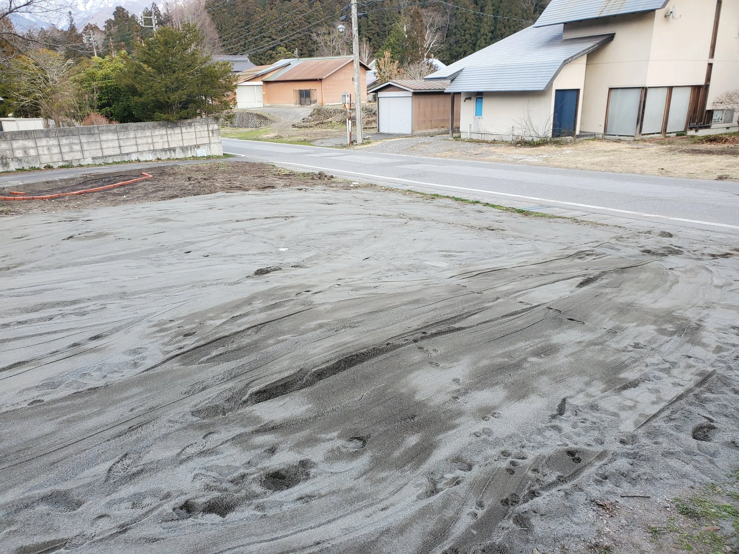 A construction area with freshly poured wet concrete in the foreground, and residential houses and trees in the background.