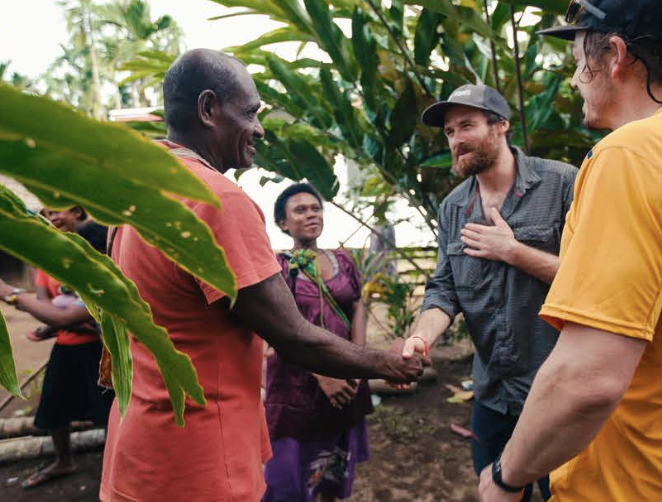 Four people standing outdoors among lush green plants, engaging in a handshake, smiling, in a West New Britain.