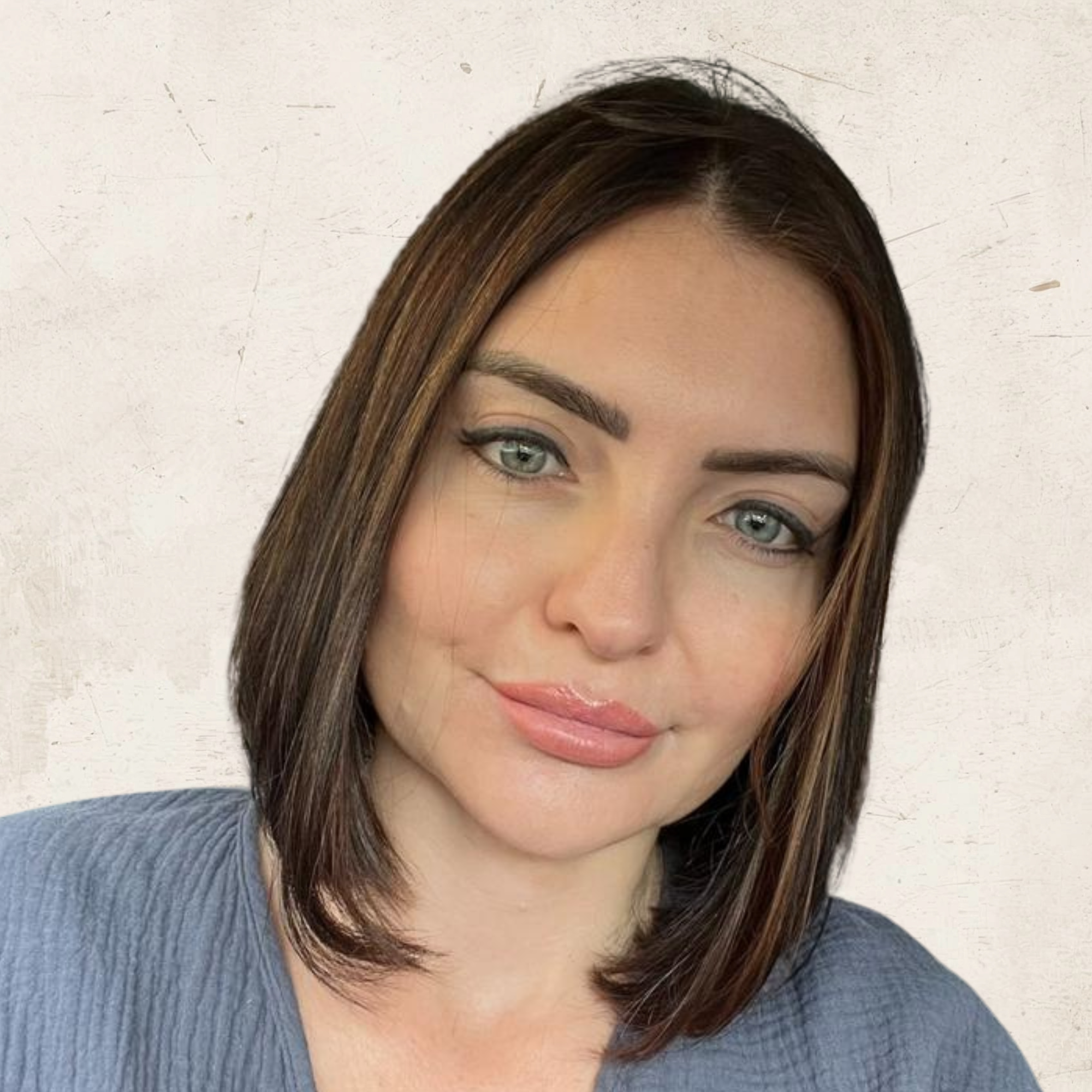 Close-up of a woman with shoulder-length brown hair, light makeup, and wearing a blue top, against a neutral background.