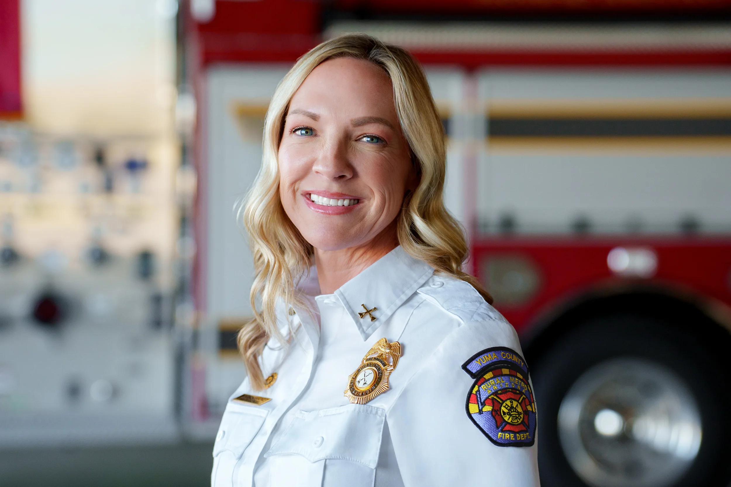 Female firefighter in uniform, smiling, standing in front of a fire truck.
