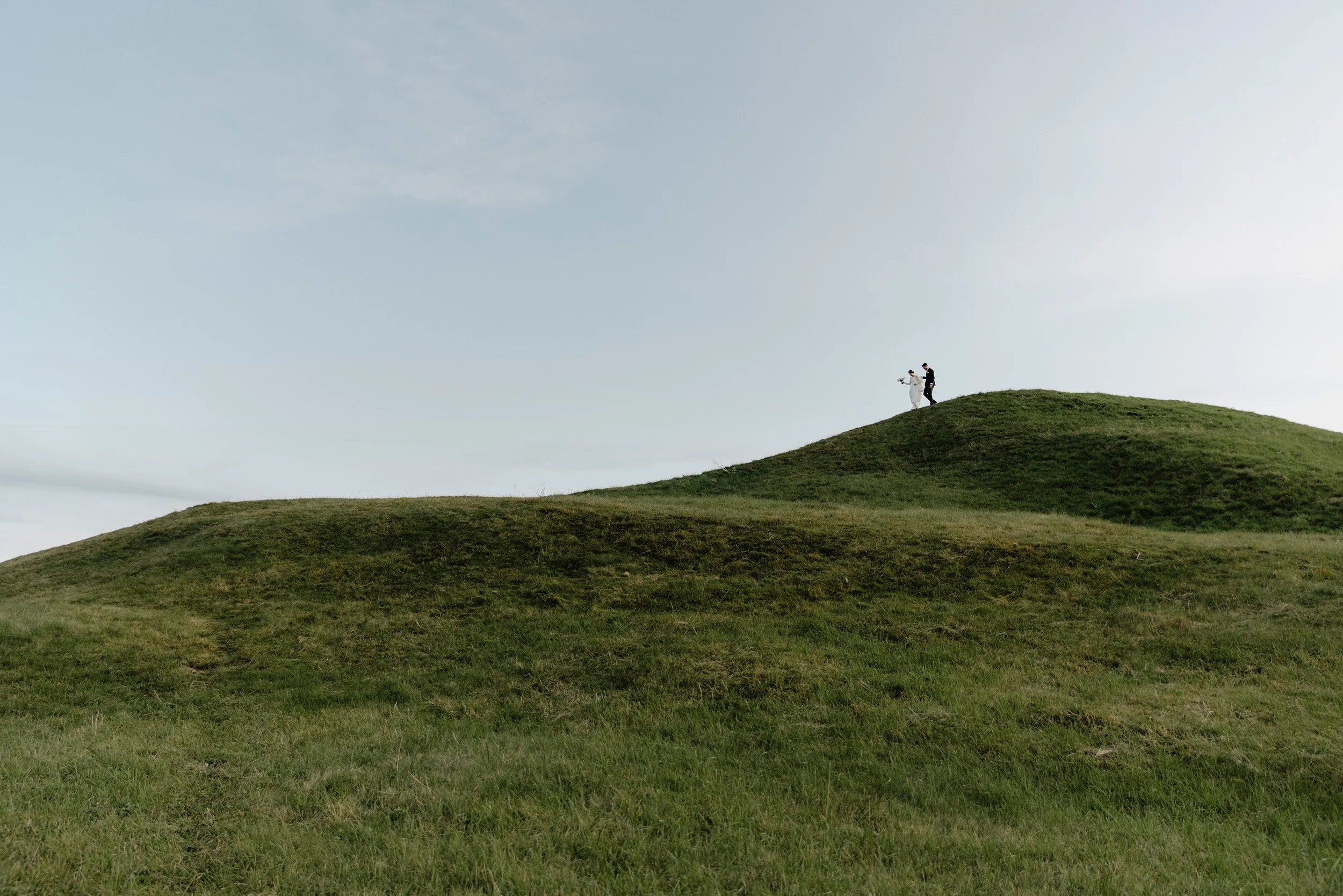 Ett bröllopspar står på en grön kulle på en öppen landsbygd under en bröllopsfotografering i Uppsala.