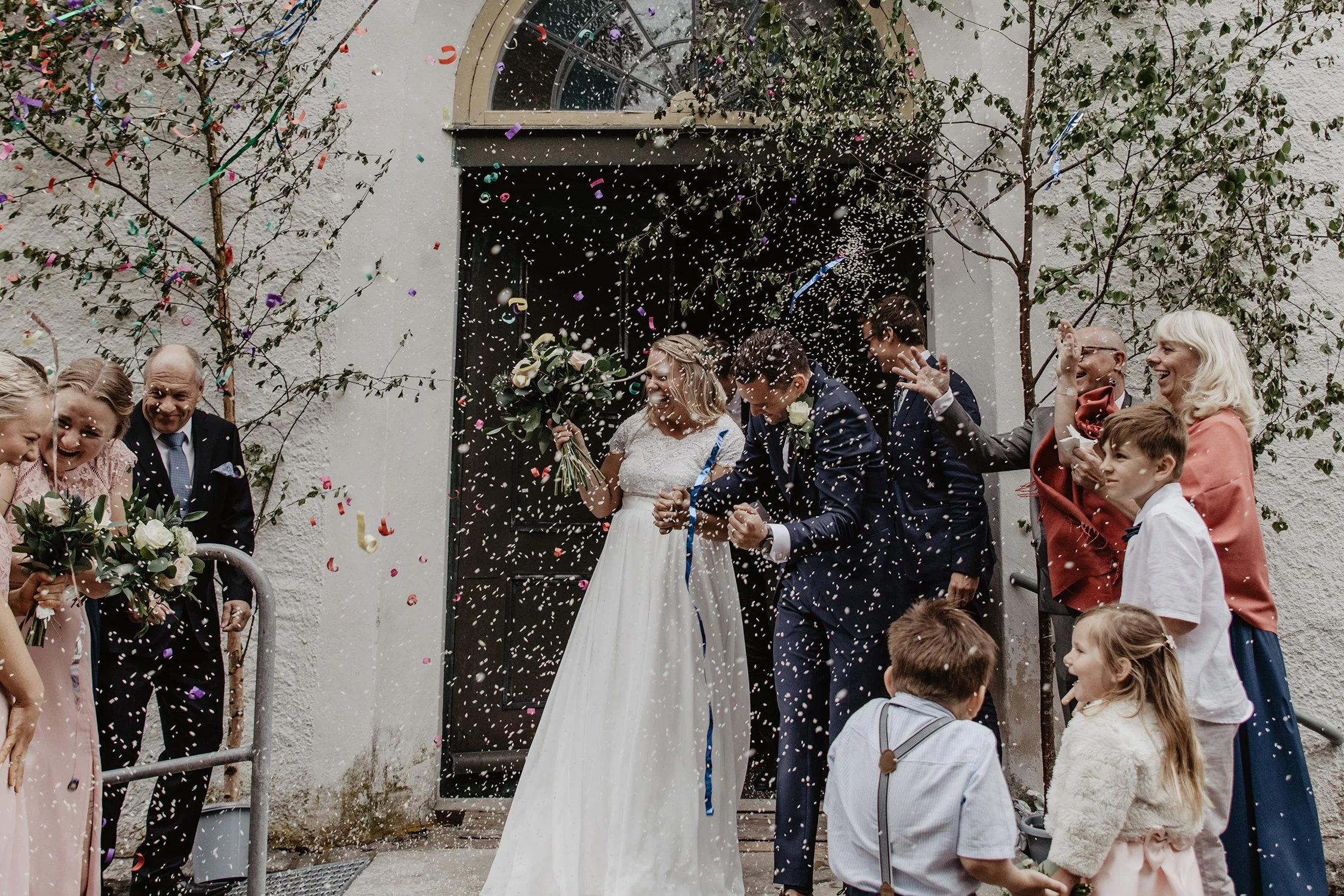 En brud och brudgum firas utanför kyrkan i Jönköing, omgiven av gäster som kastar konfetti och firar.