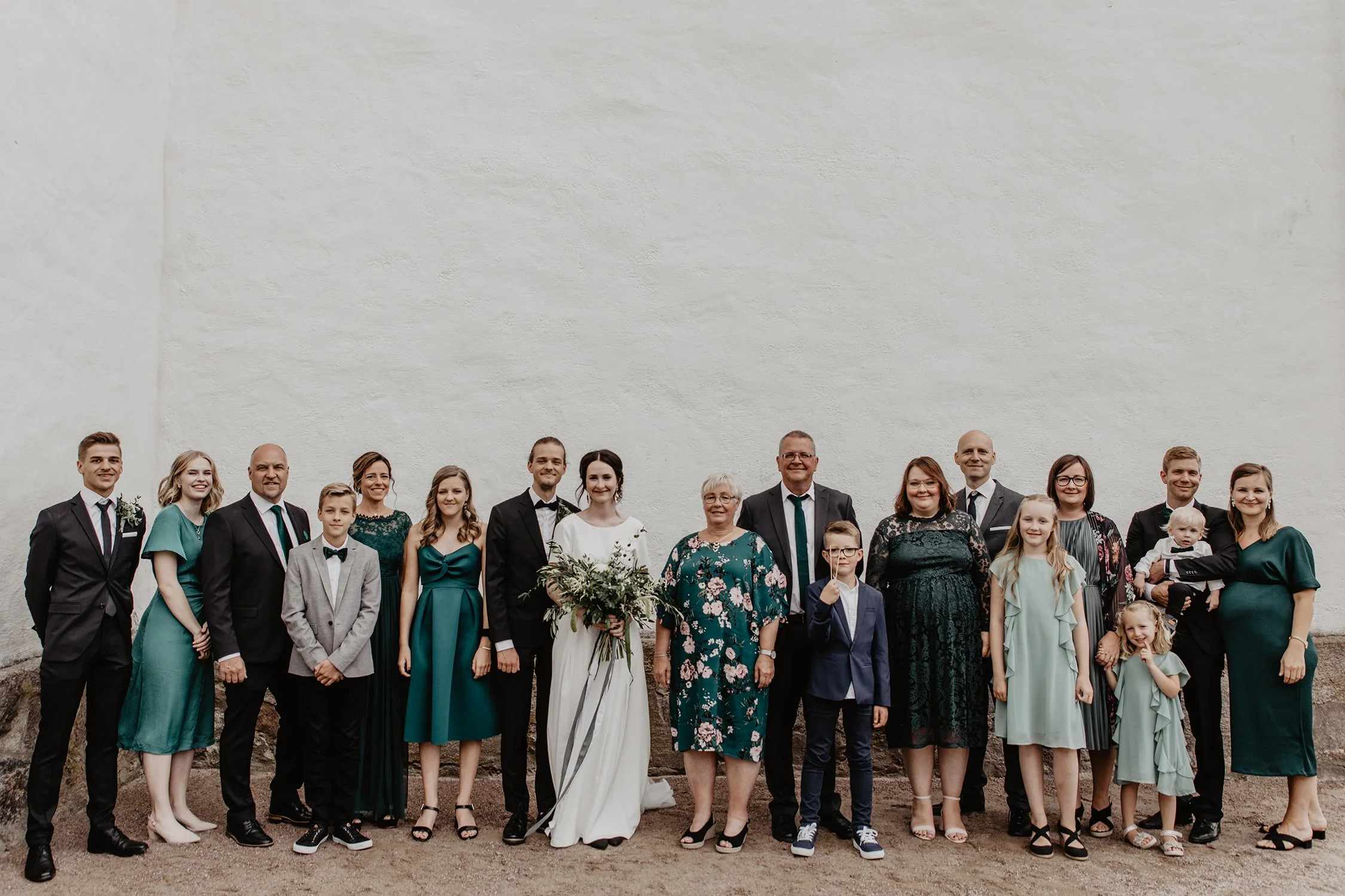 En familjebild efter vigseln med brudparet i mitten framför en vit vägg under en bröllopsfotografering i Sävsjö.
