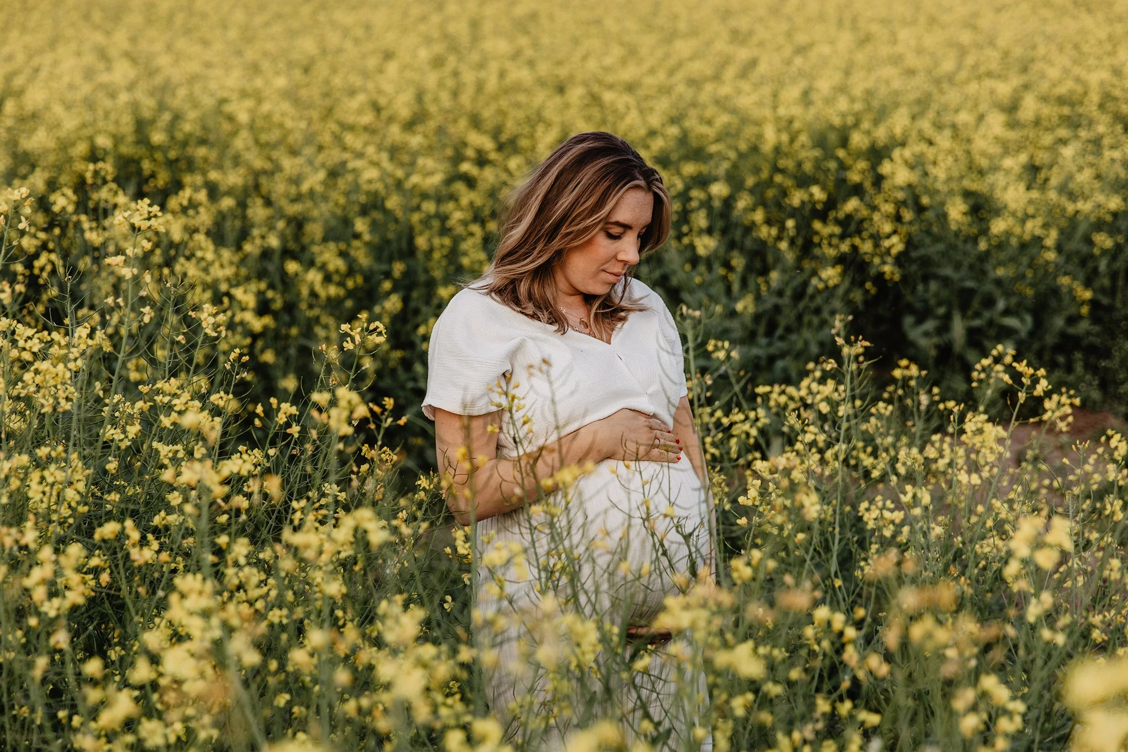En gravid kvinna som håller sin mage i en gul blomsteräng.