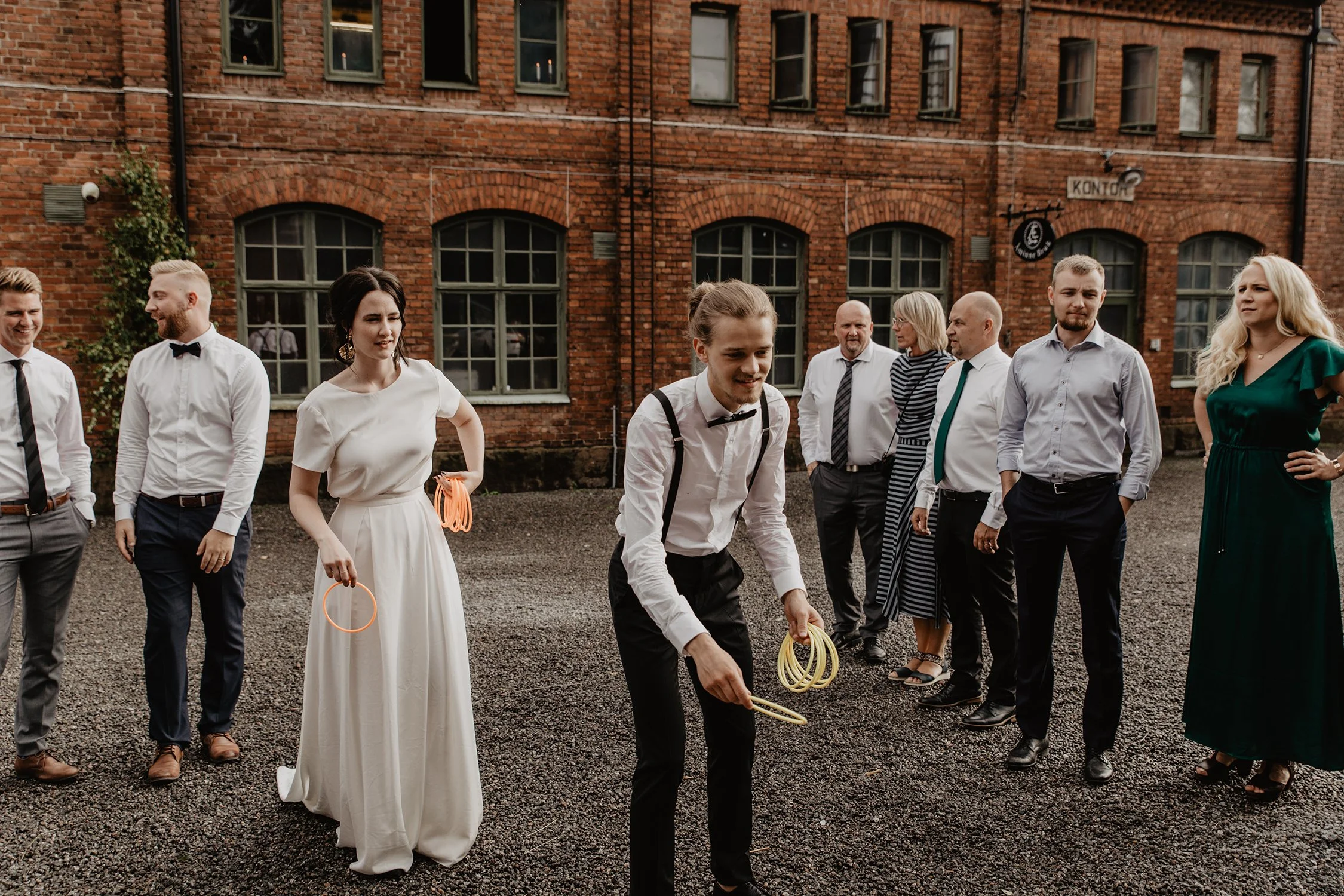 En grupp människor utanför Åminne Bruk som är klädda i festkläder står framför en röd tegelvägg, med några personer som håller neonfärgade armband.