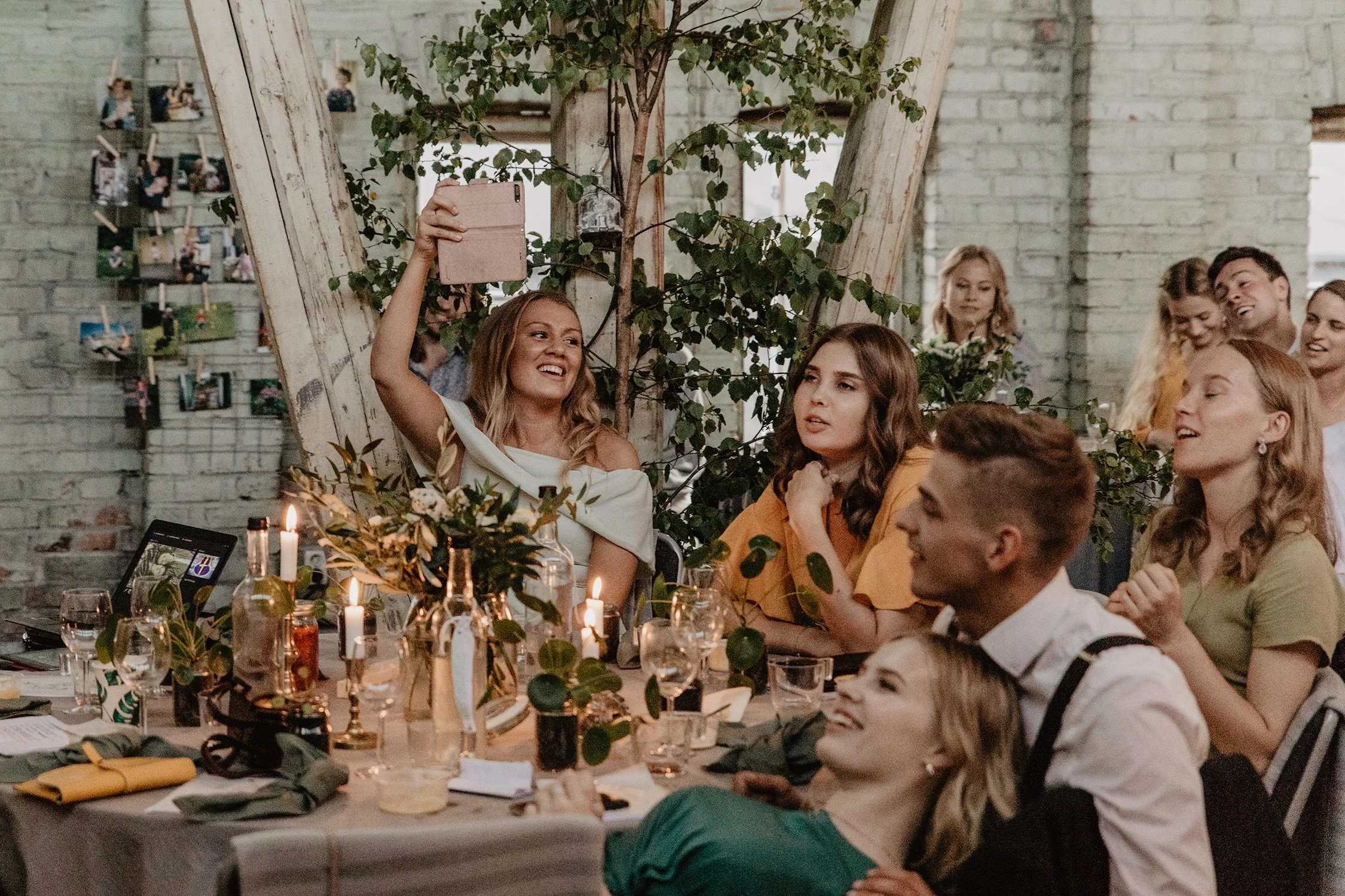 Grupp människor vid ett festbord, firar, med ljus, blommor och mat, i ett industriellt inrett Åminne Bruk.