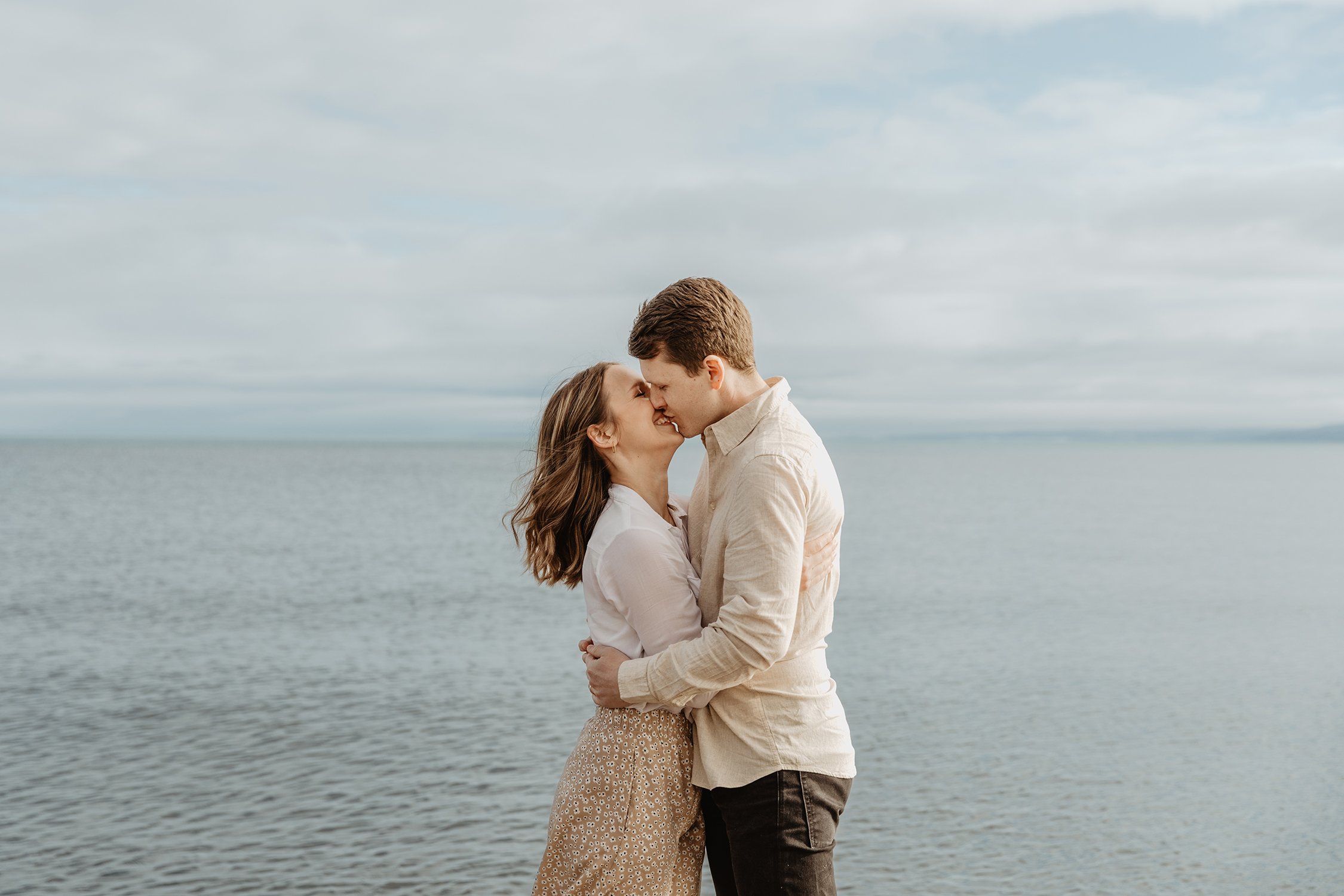 En ung man och kvinna kysser varandra nära en sjö, omgivna av ett molnigt himmel.