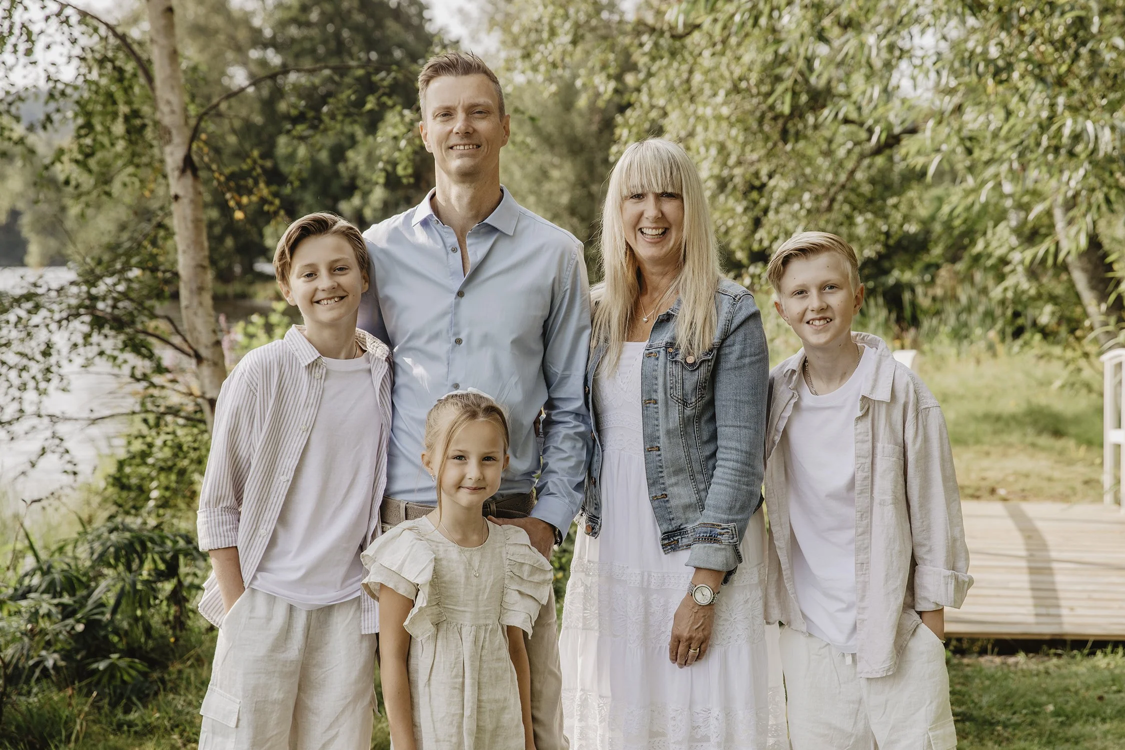 En grupp familjemedlemmar står utomhus i ett grönt, trädfyllt område, alla ler och ser glada ut.