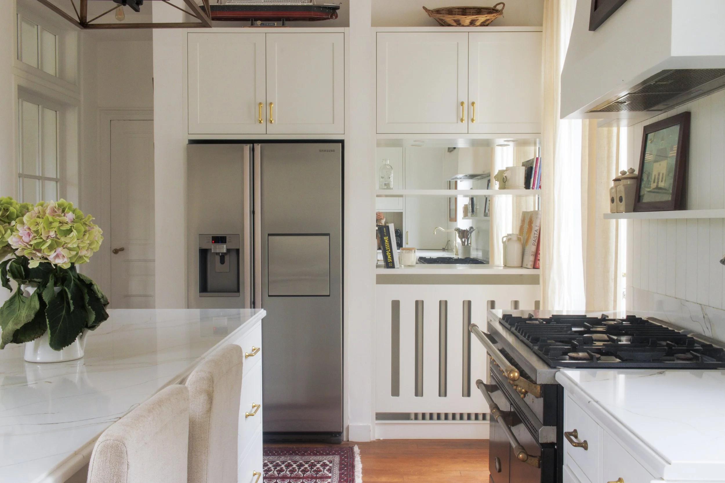 A kitchen with white cabinets, a stainless steel fridge, a stove, and decorative items on shelves and counters, including a vase of pink and green flowers.