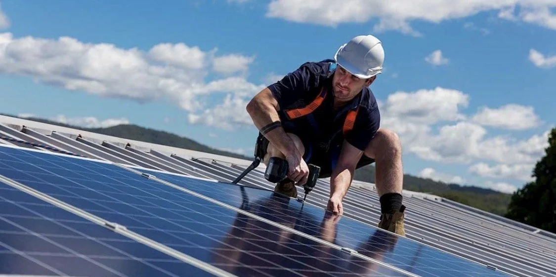 A technician installing solar panels on a roof in a rural area.