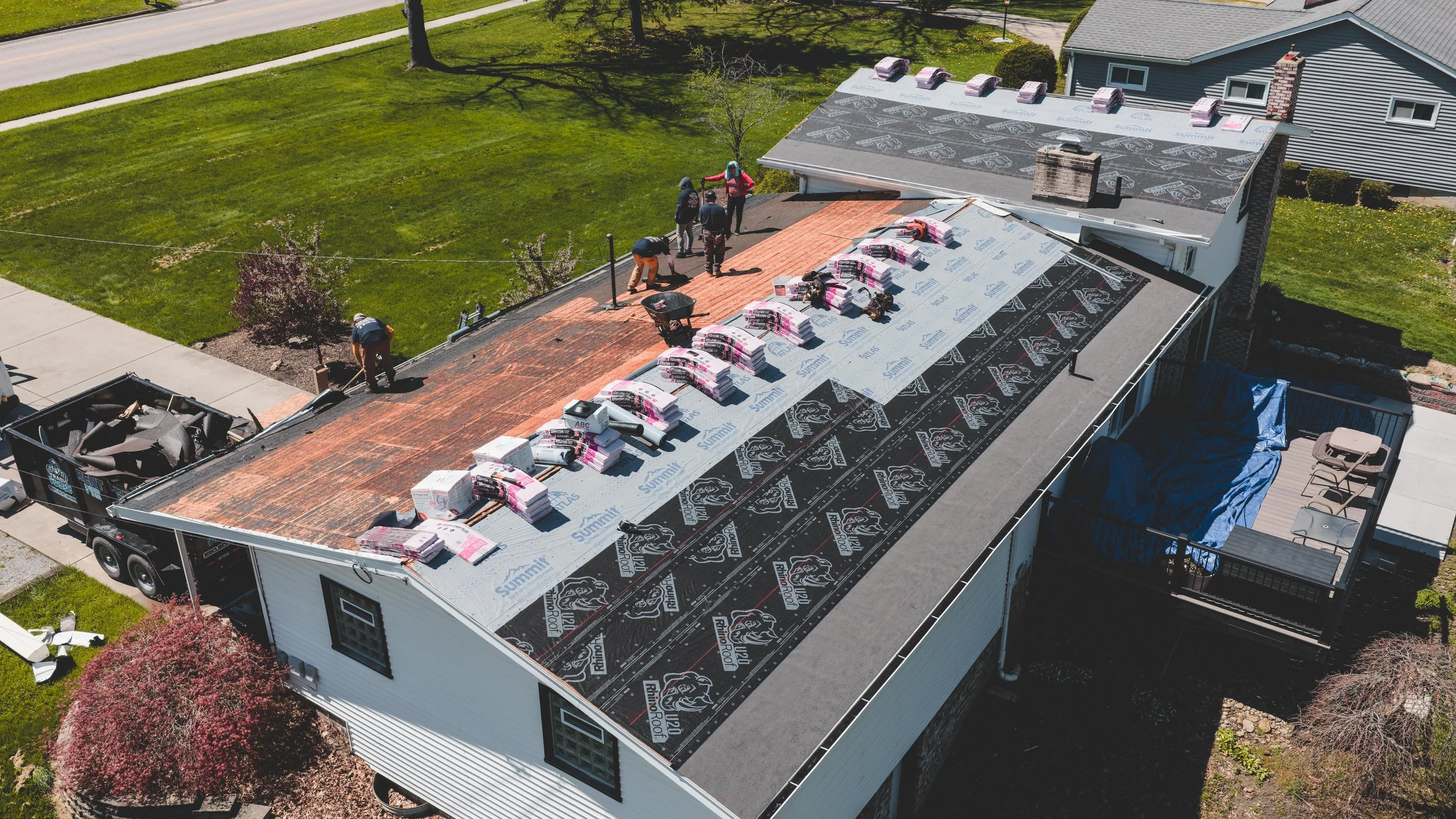 Aerial view of a residential house under construction showing workers installing a new roof with roofing materials and underlayment.