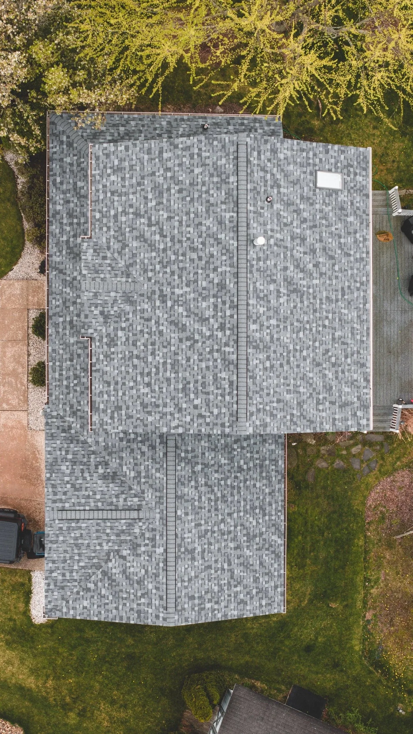 An aerial view of a house with a gray shingle roof surrounded by trees and a green yard.