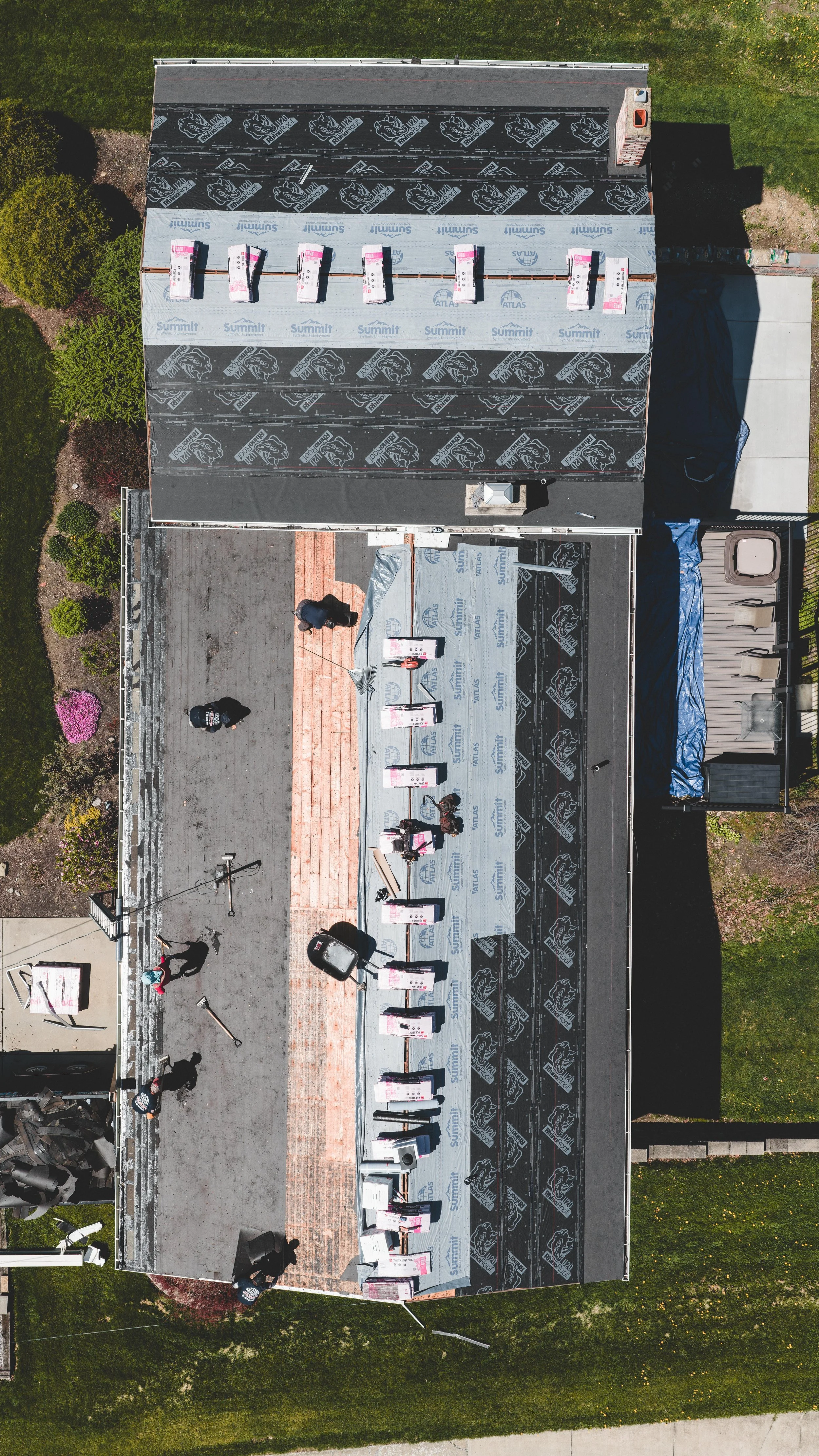 An aerial view of a house roof during renovation, showing workers installing roofing materials and tools.