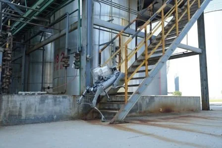 An industrial exterior with a staircase, a robot, and some machinery.