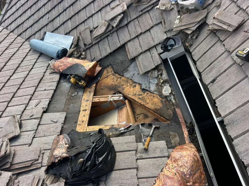 roof with missing shingles, exposed wooden framework, and construction tools near an opening in the roof.