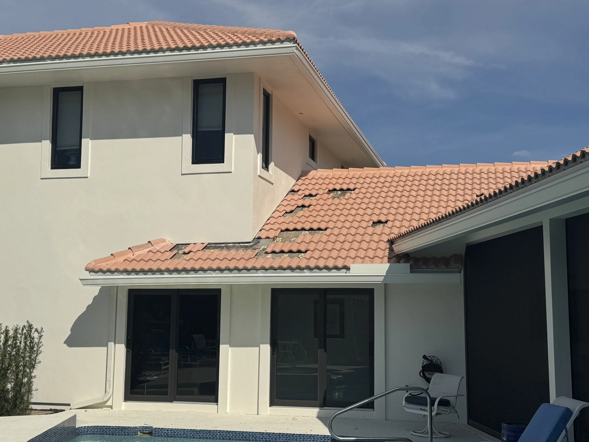 View of the exterior of a multi-story house with beige walls and terracotta tile roof, featuring multiple windows and sliding glass doors, with a swimming pool in the foreground.