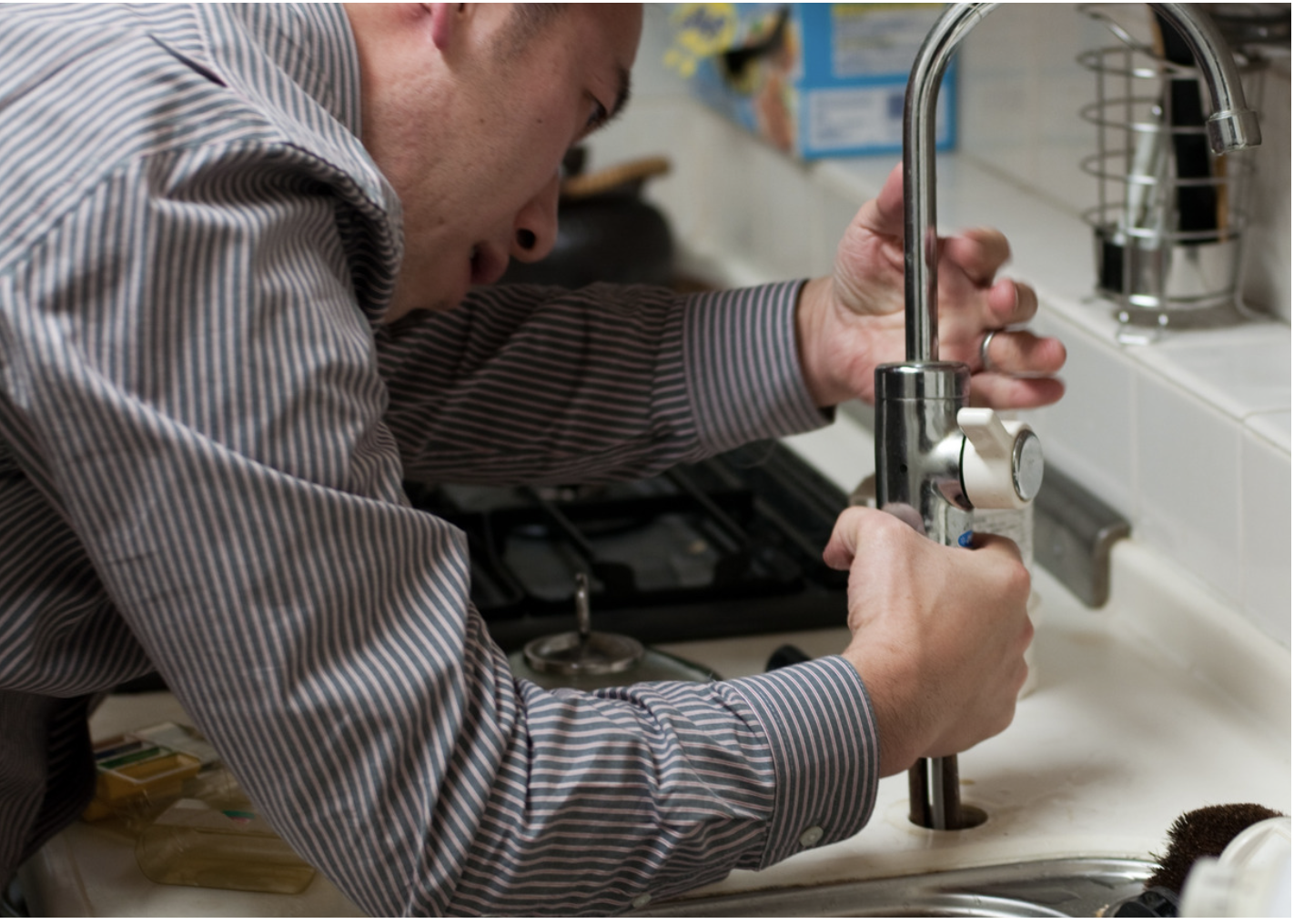A man fixing a sink faucet in a kitchen.